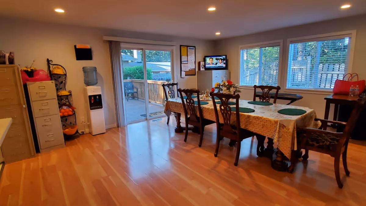 Bright dining room with a long table and chairs, hardwood floors, windows, and a sliding glass door to a deck.