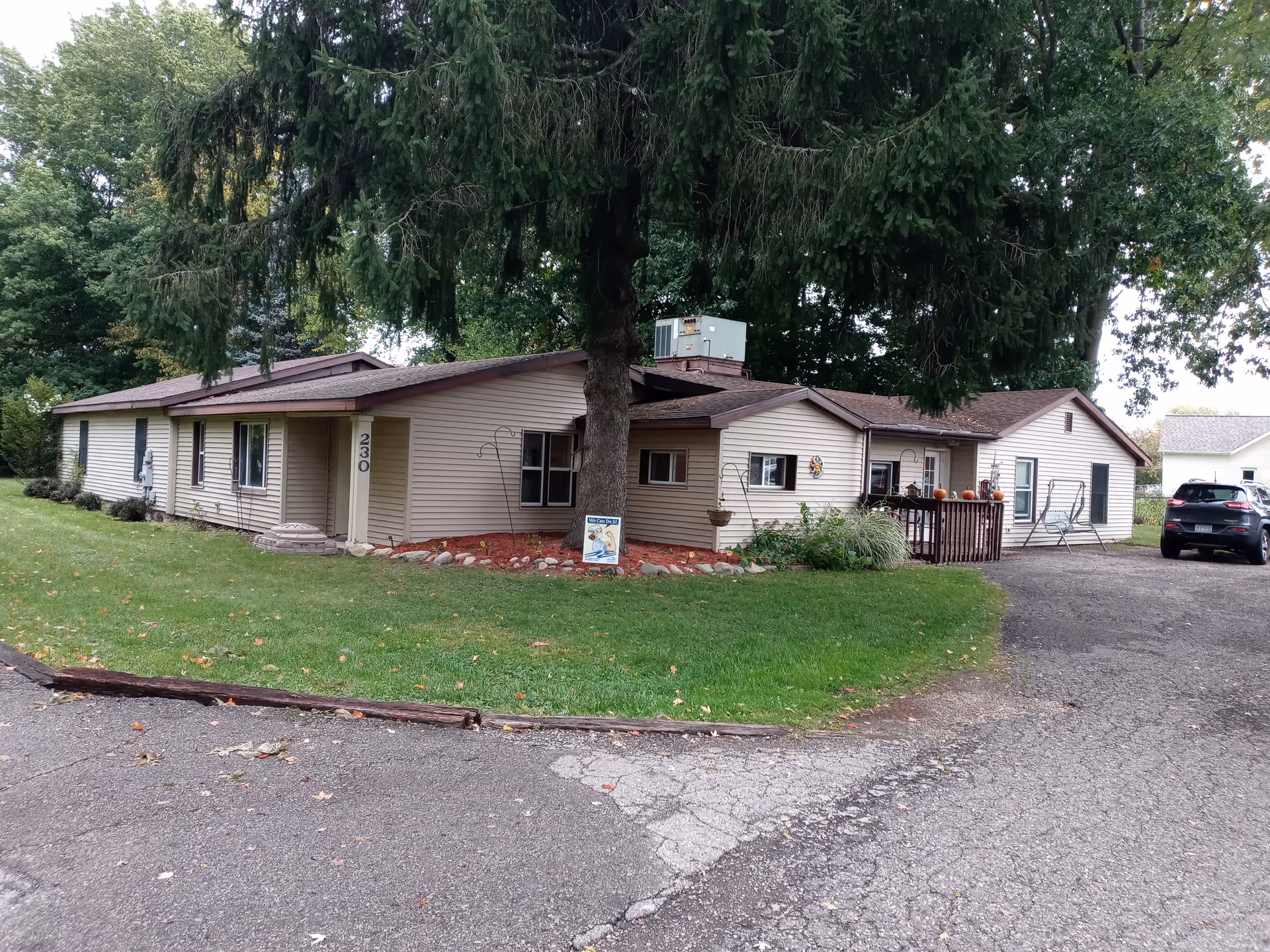 Single-story beige facility with a large tree in front and a driveway.