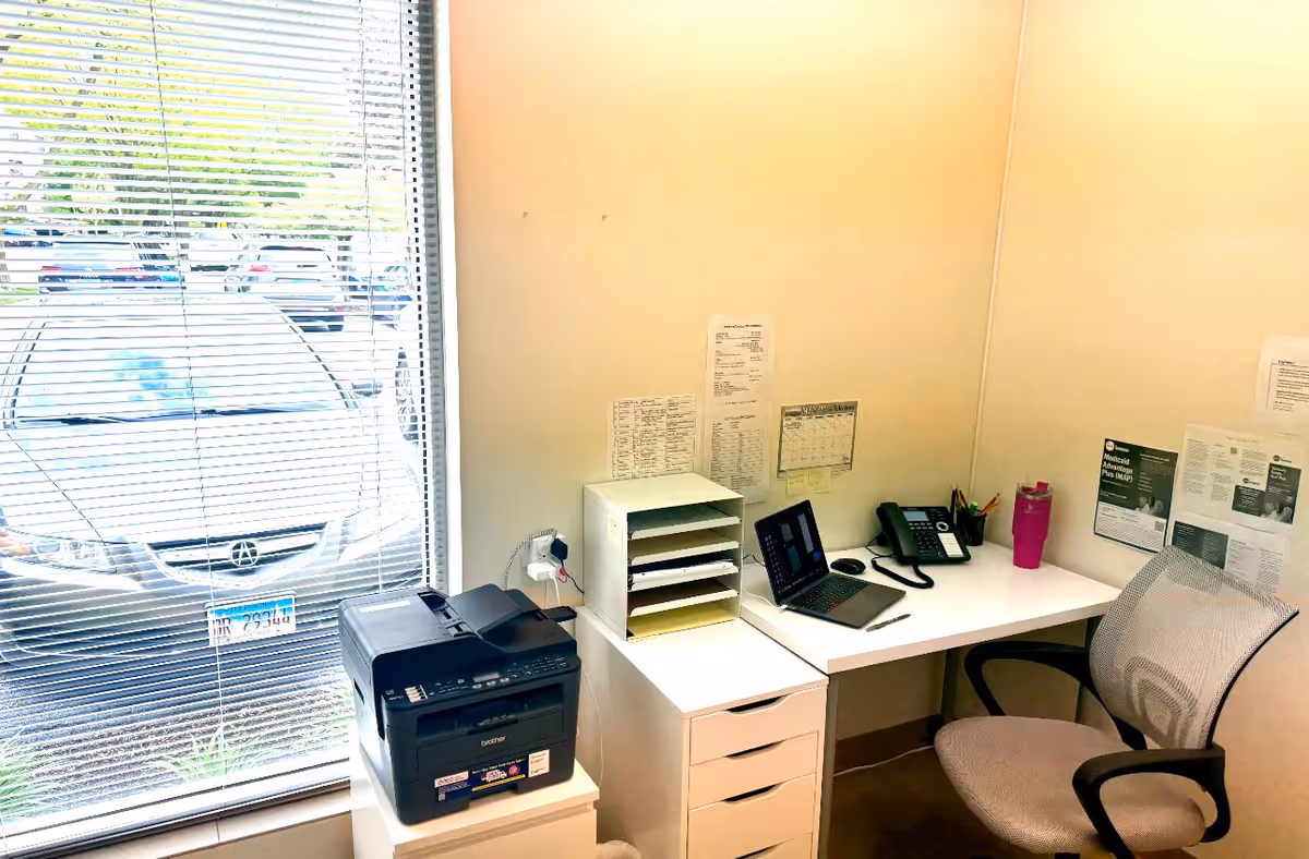 Interior office area with a desk, laptop, printer, filing organizer, and wall notices.