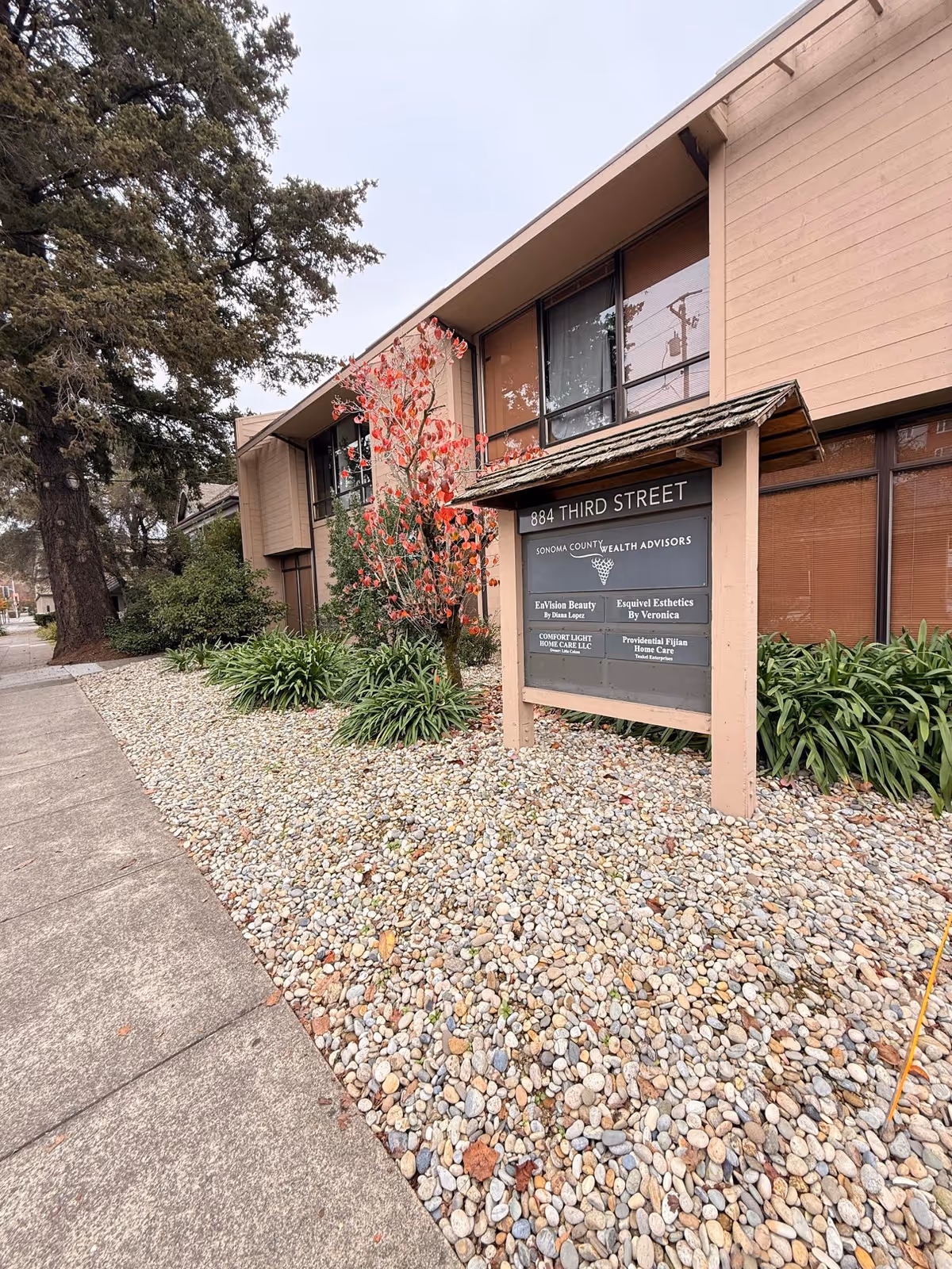 Exterior of a tan, two-story building with large windows, signboard, and rock landscaping.