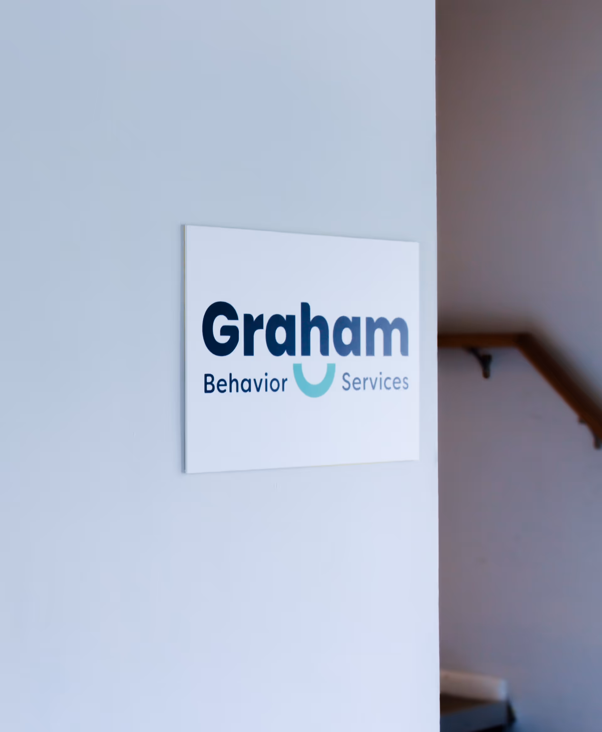 Interior wall displays Graham Behavior Services sign next to a stair railing.