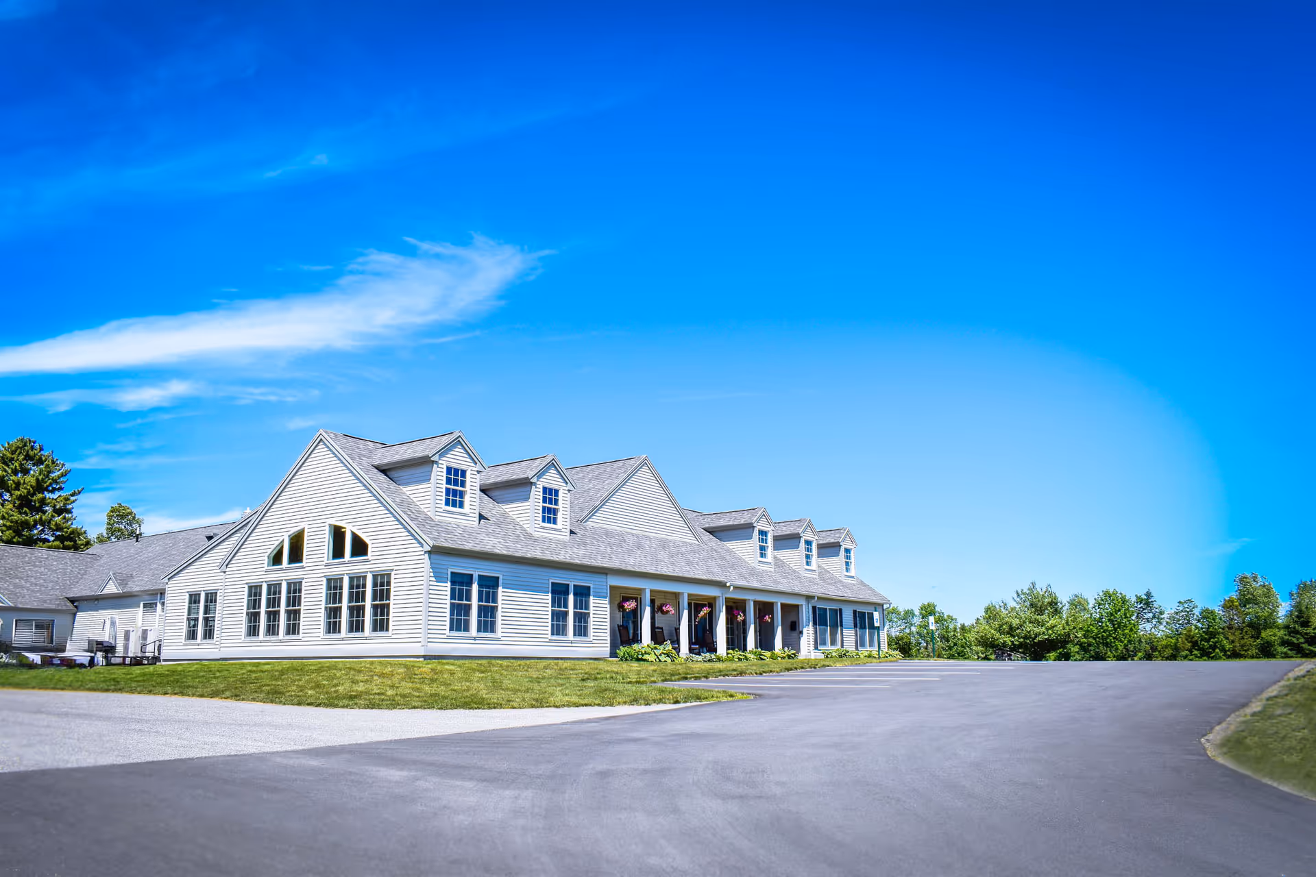 White Pleasant Meadows Estates senior living building with a long curved driveway and blue sky.