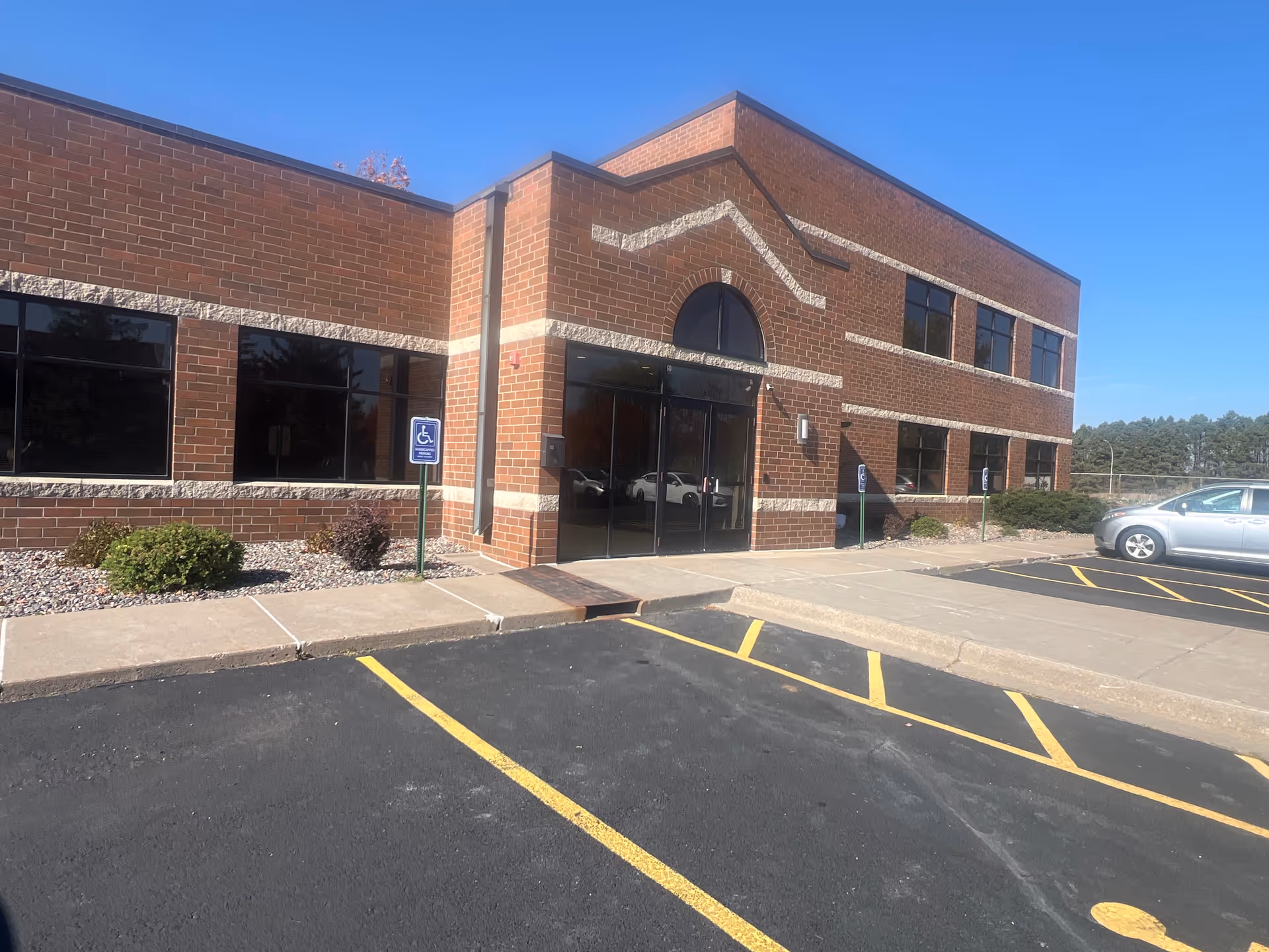 Brick senior living facility exterior with glass entrance and parking lot.