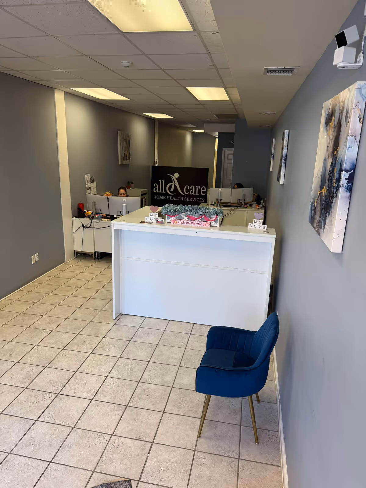 Interior reception area featuring a white front desk, staff at computers, blue chairs.