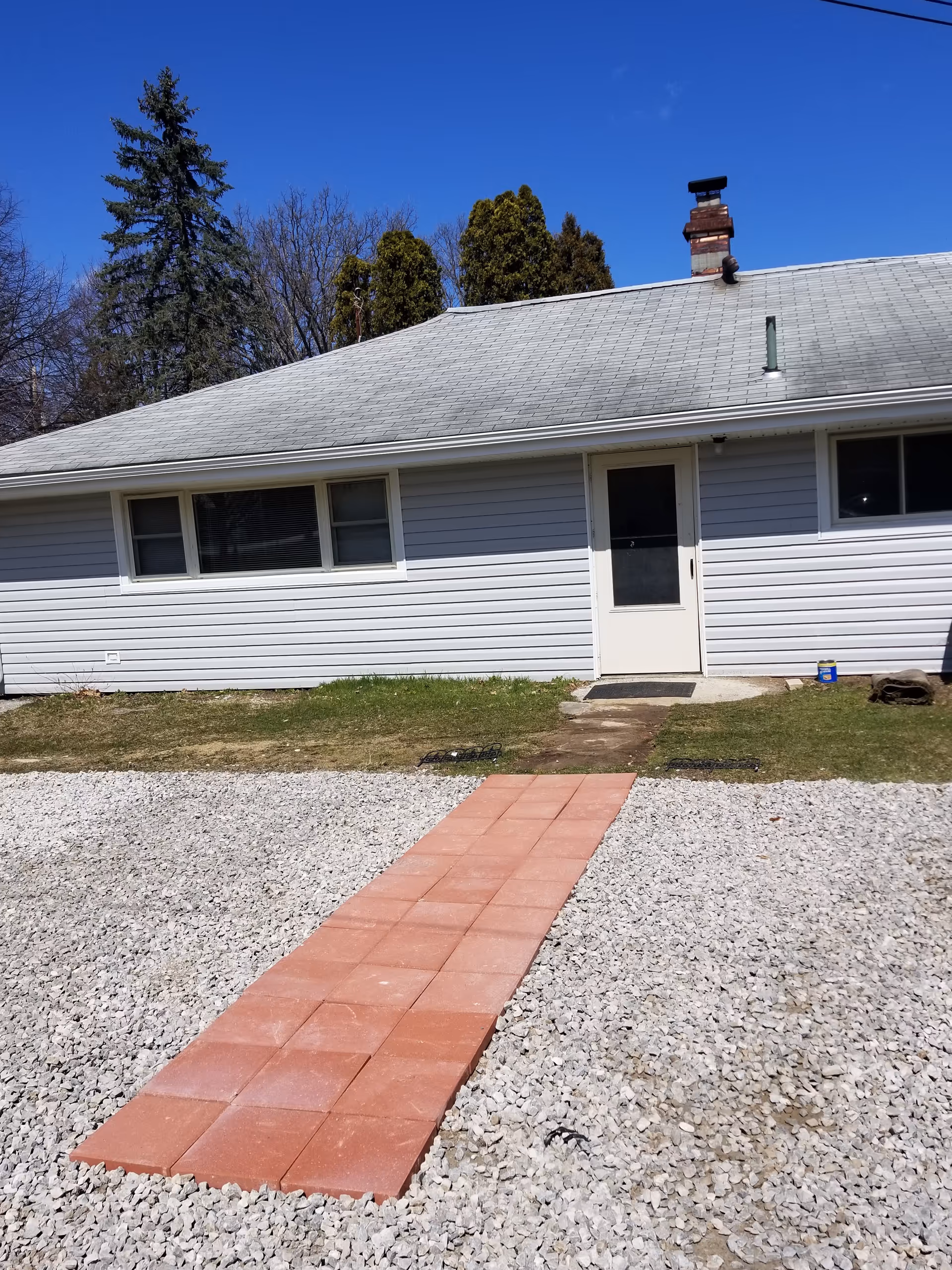 Exterior view of a single-story building with a red tile walkway leading to a white door.