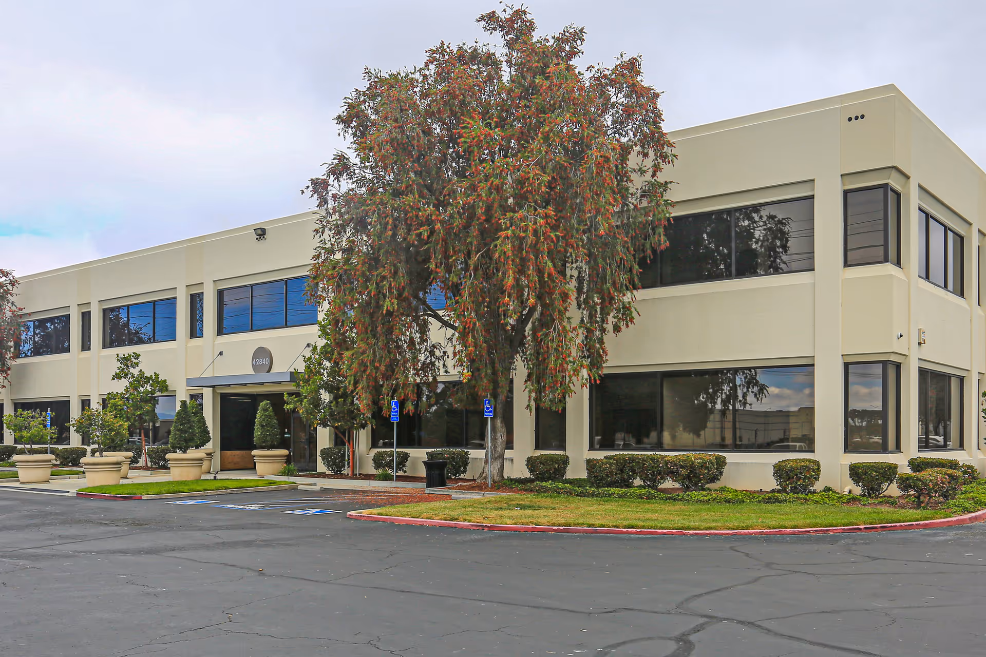 A beige two-story building with large windows and a landscaped front entrance.