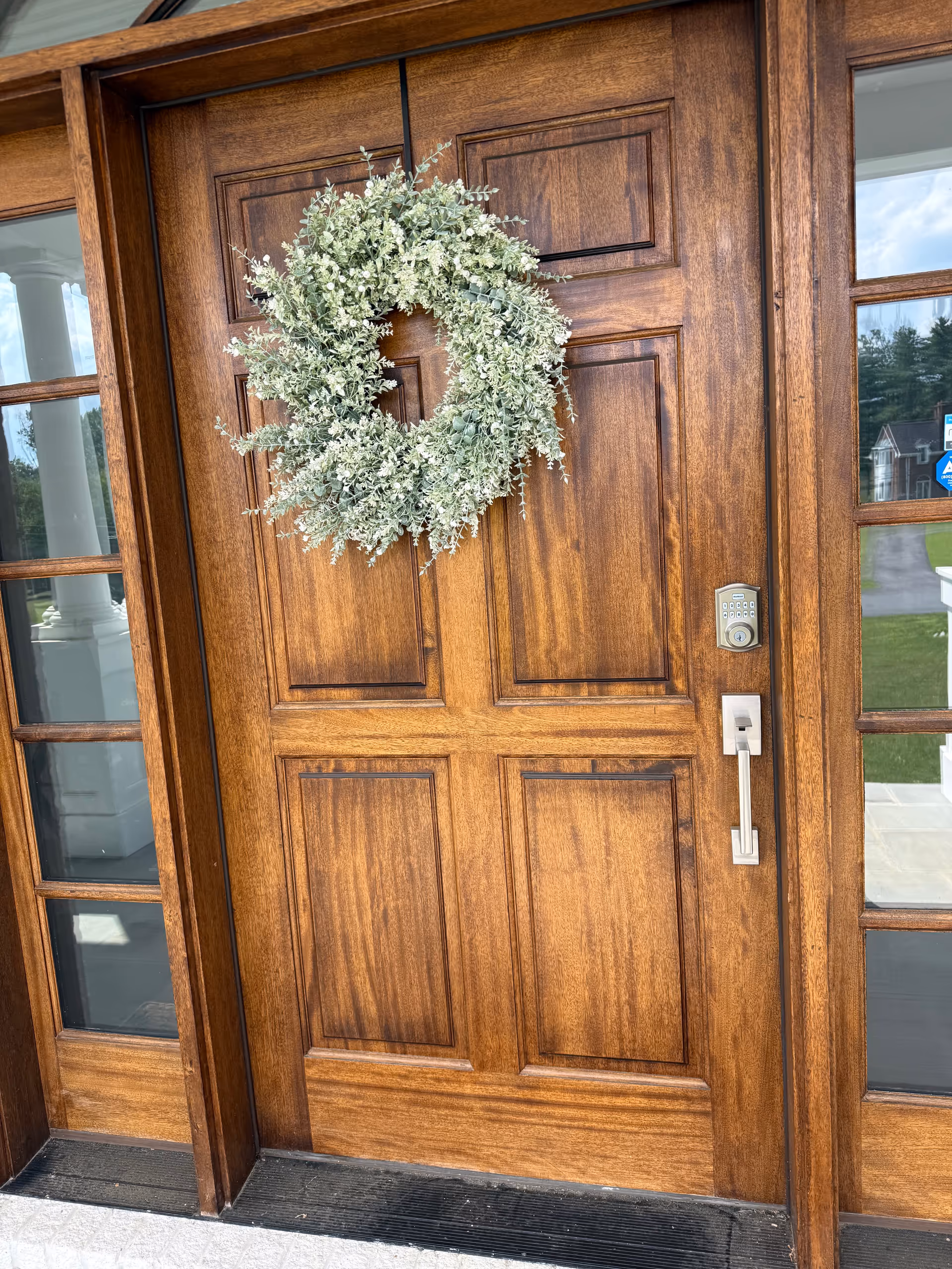 Wooden front door with a greenery wreath, sidelights, and a keypad lock.