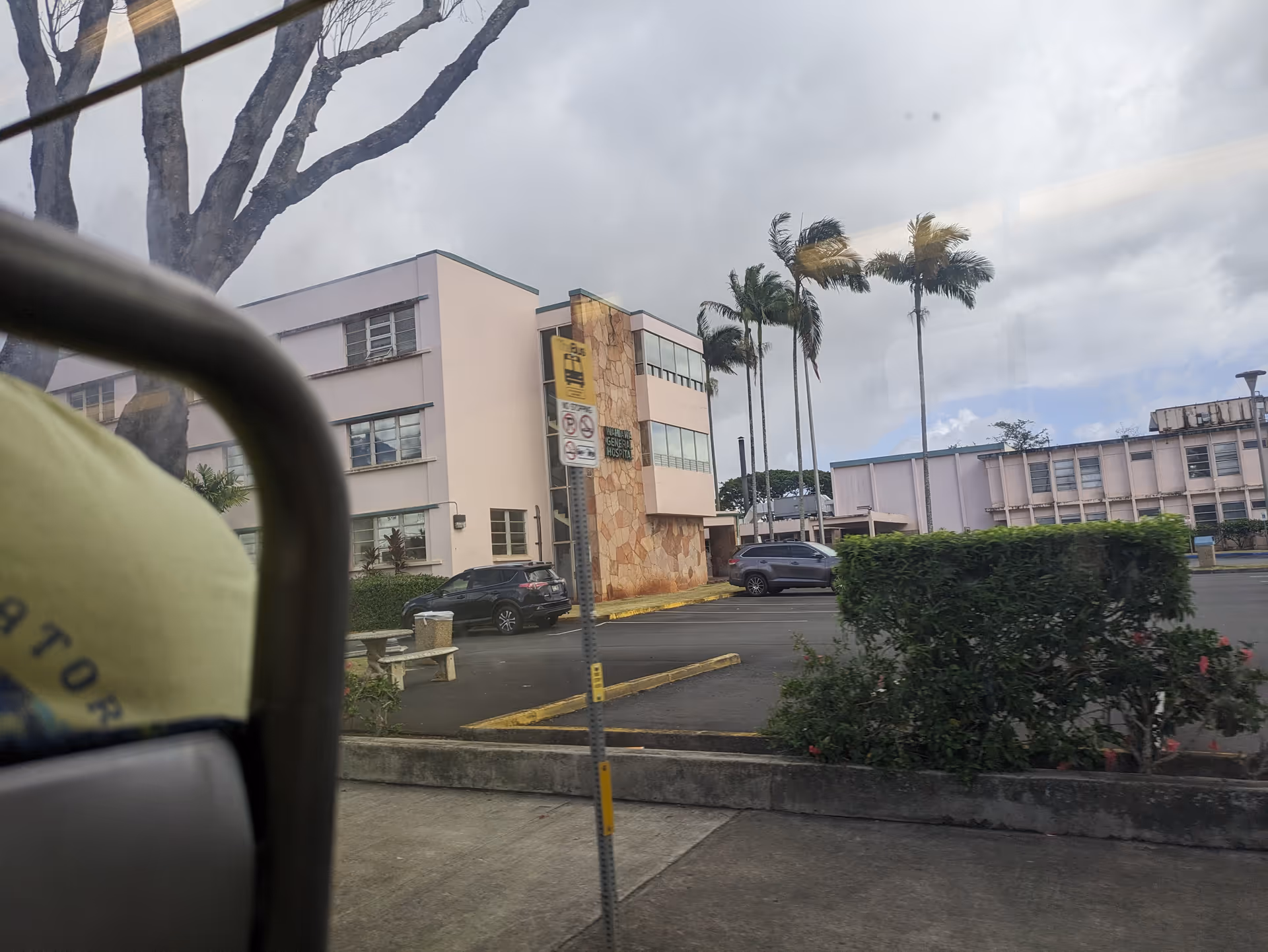 Exterior view of The Queen’s Medical Center Wahiawā with palm trees and parked cars.