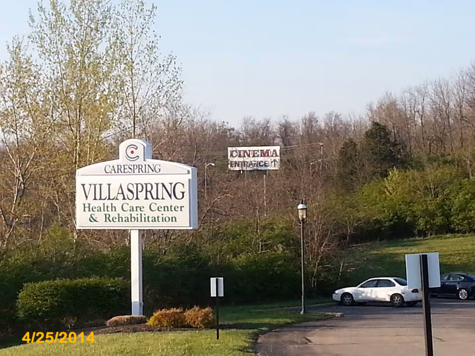 Exterior view of Villaspring Health Care Center sign near trees and parked cars.