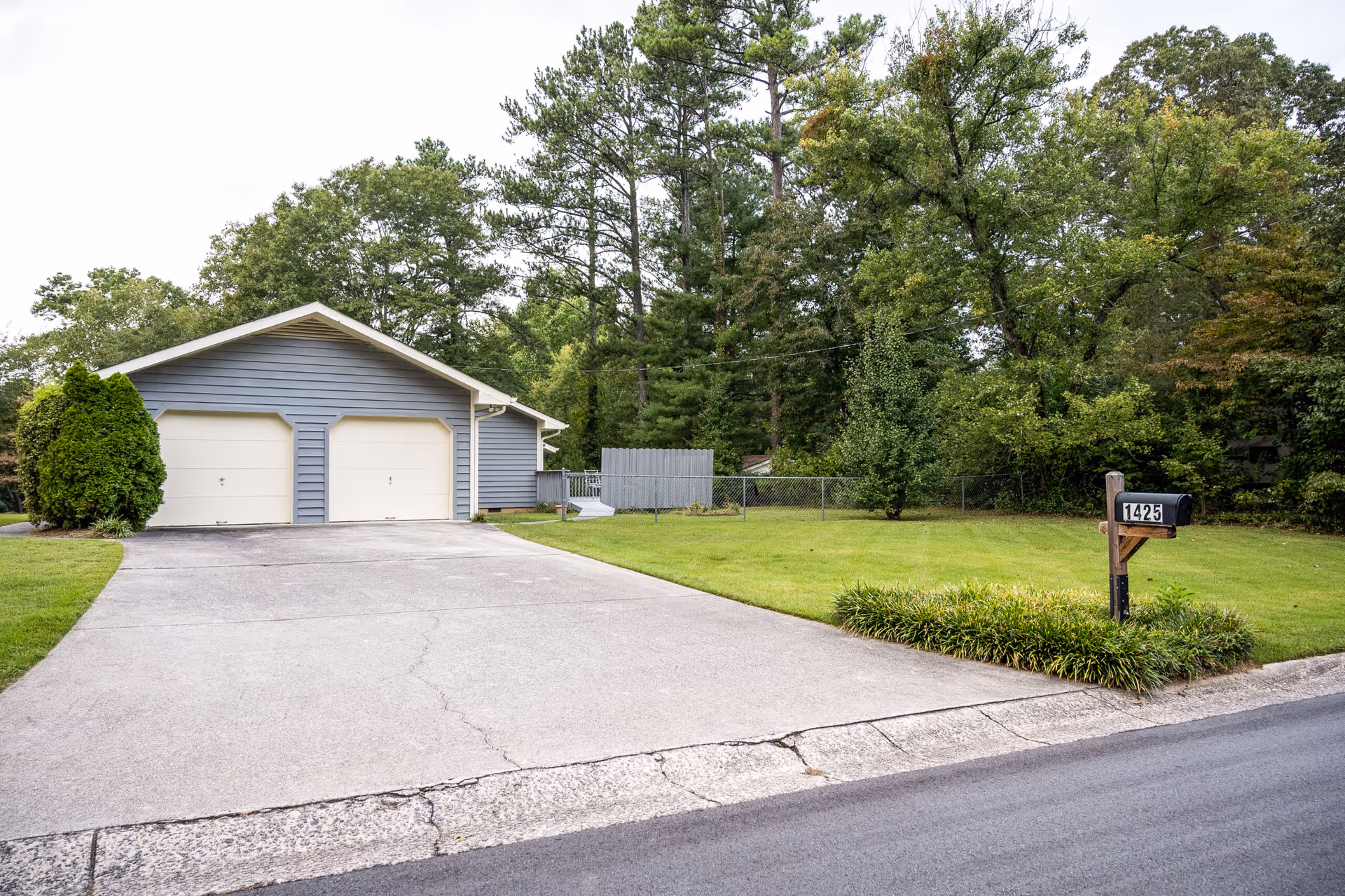 Blue two-garage building with driveway, green lawn, and mailbox near curb.