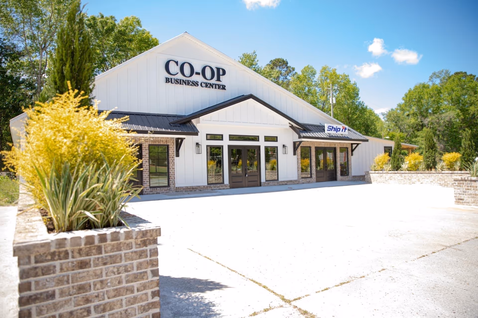 White building with CO-OP Business Center sign, surrounded by trees and brick planters.
