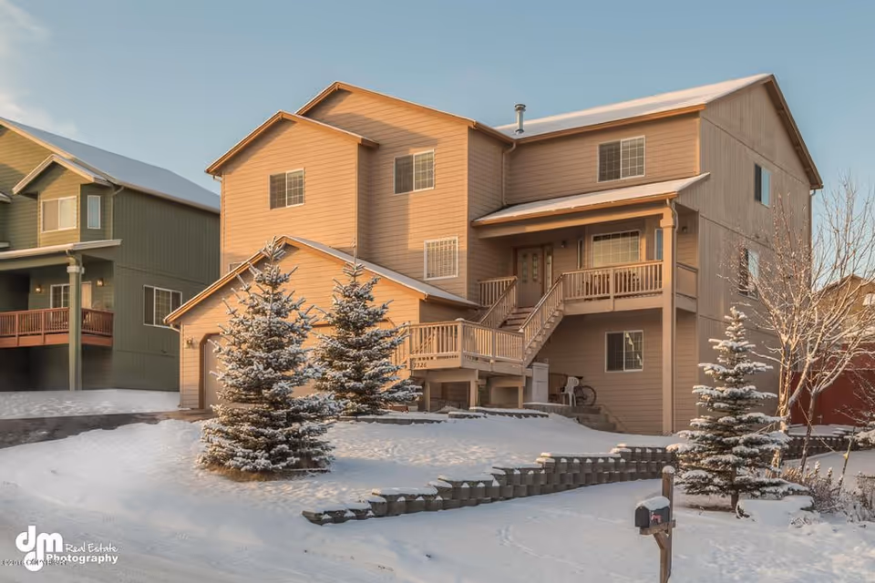 Two-story beige senior living home with snow-covered lawn and evergreen trees in front.