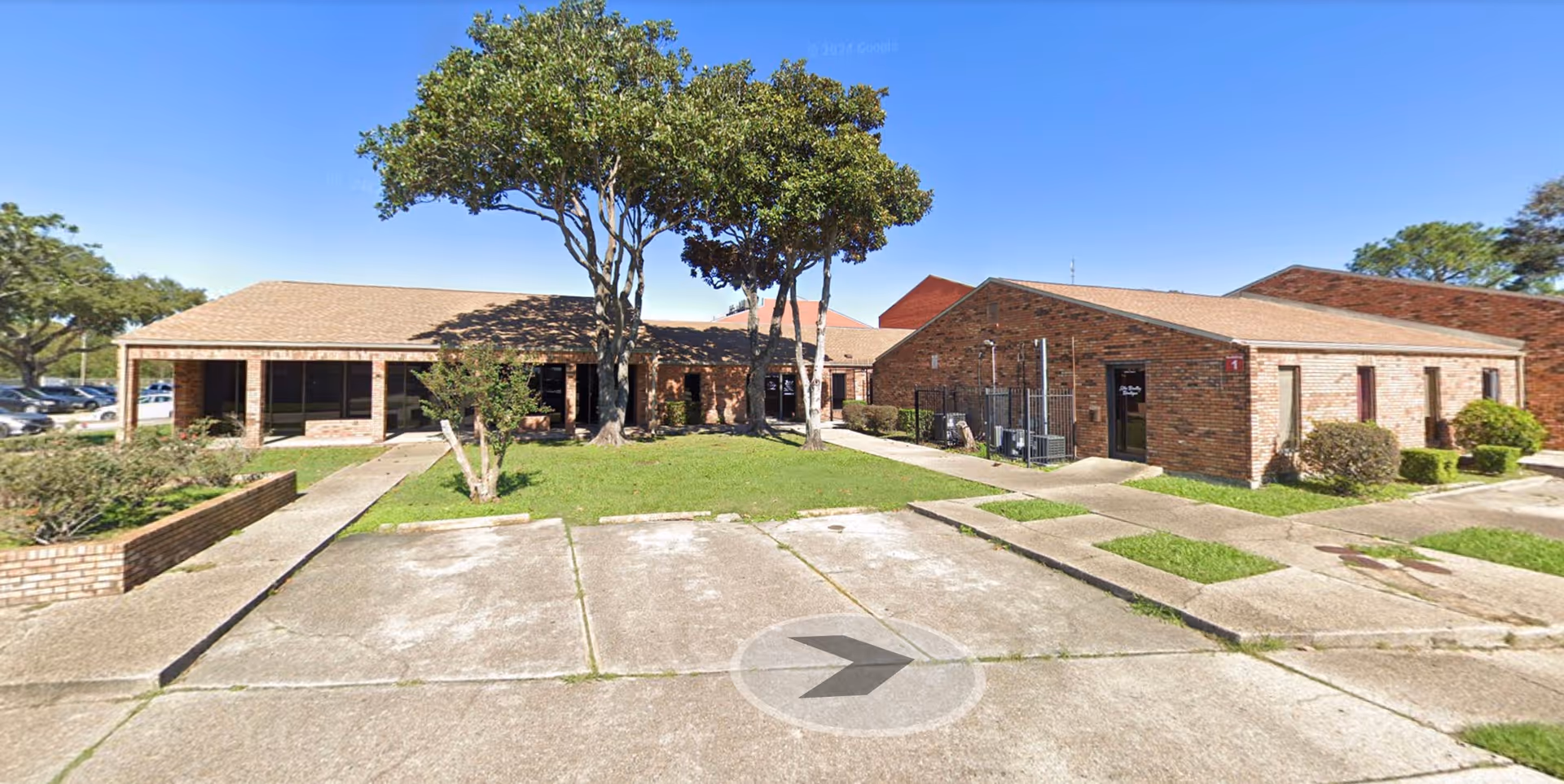 Brick senior living facility exterior with front lawn, trees, and sidewalk.