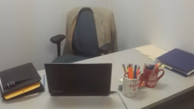 Office desk with laptop, folders, pens, and a chair with a jacket draped over it.