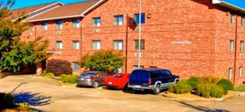 Front view of a brick senior living building with parked cars and manicured shrubs.