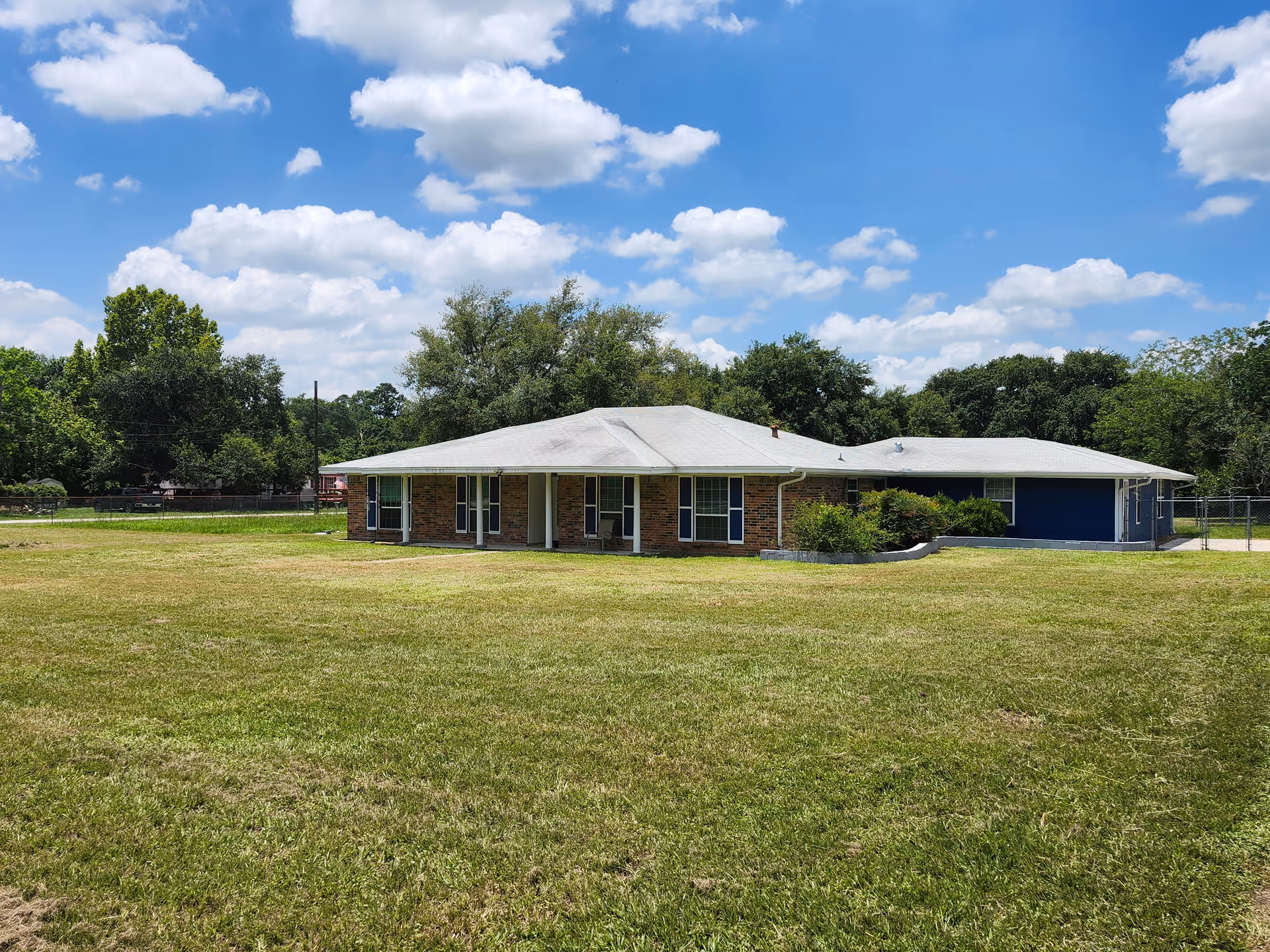 A single-story brick building with a light roof sits on a grassy field under blue skies.