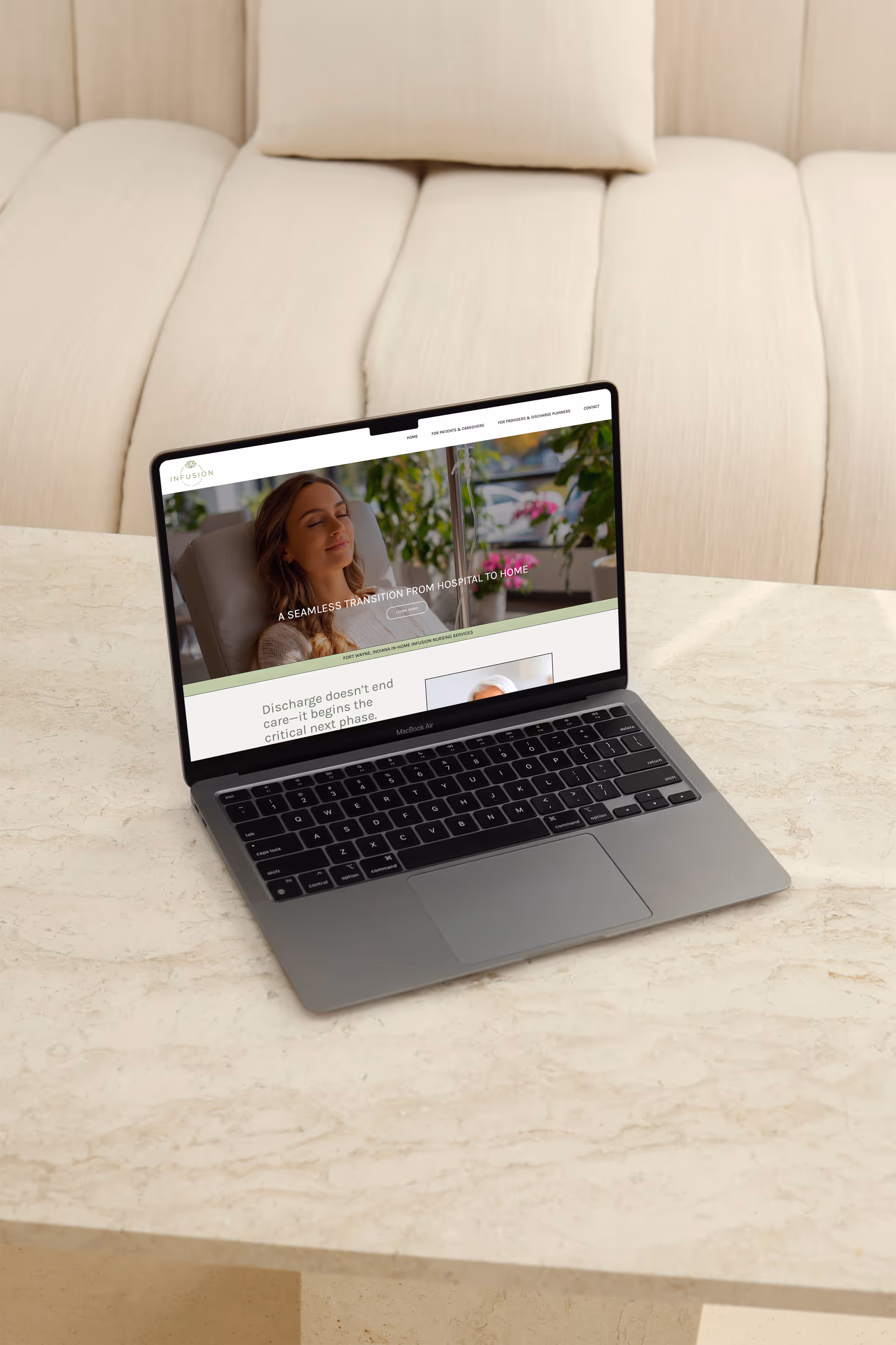 Open laptop on a marble table displays a caregiving website, with a beige couch in background.