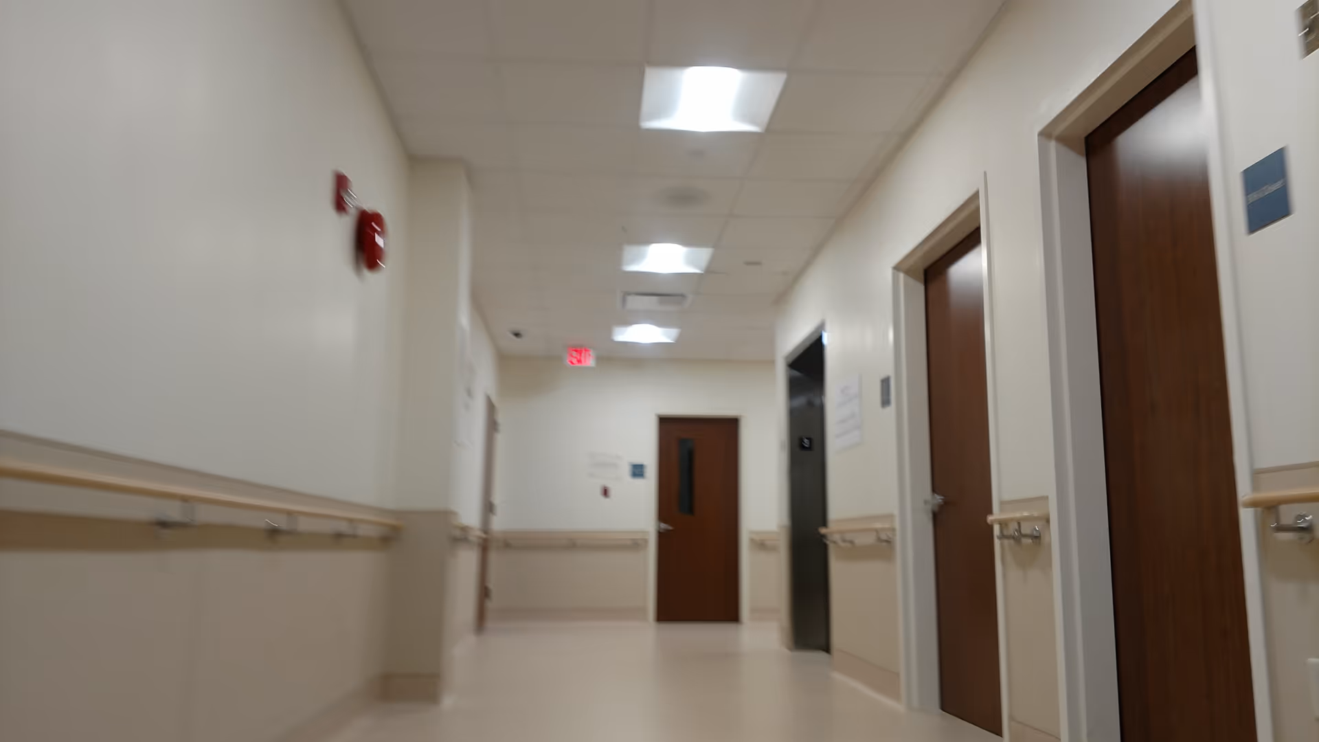 Long hallway in a senior living facility with doors, handrails, and ceiling lights.