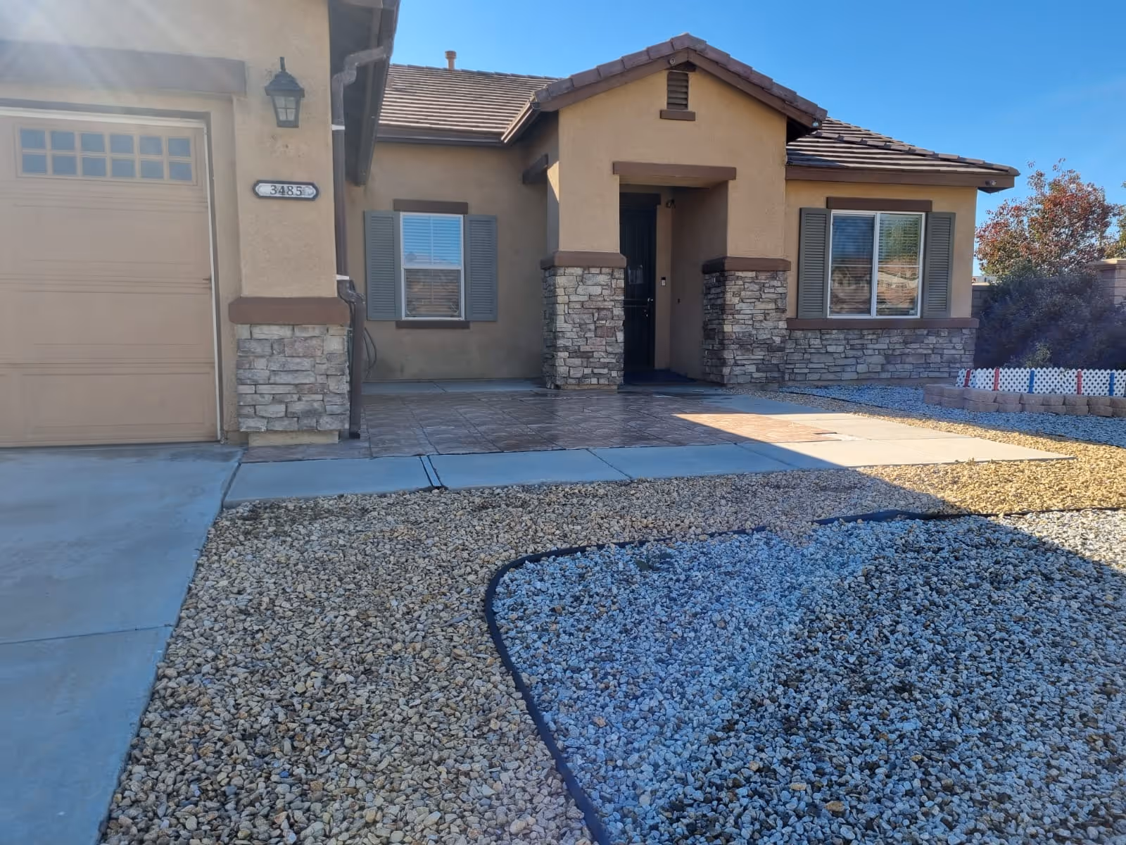 Front exterior of a single-story home with stone accents and a gravel yard.