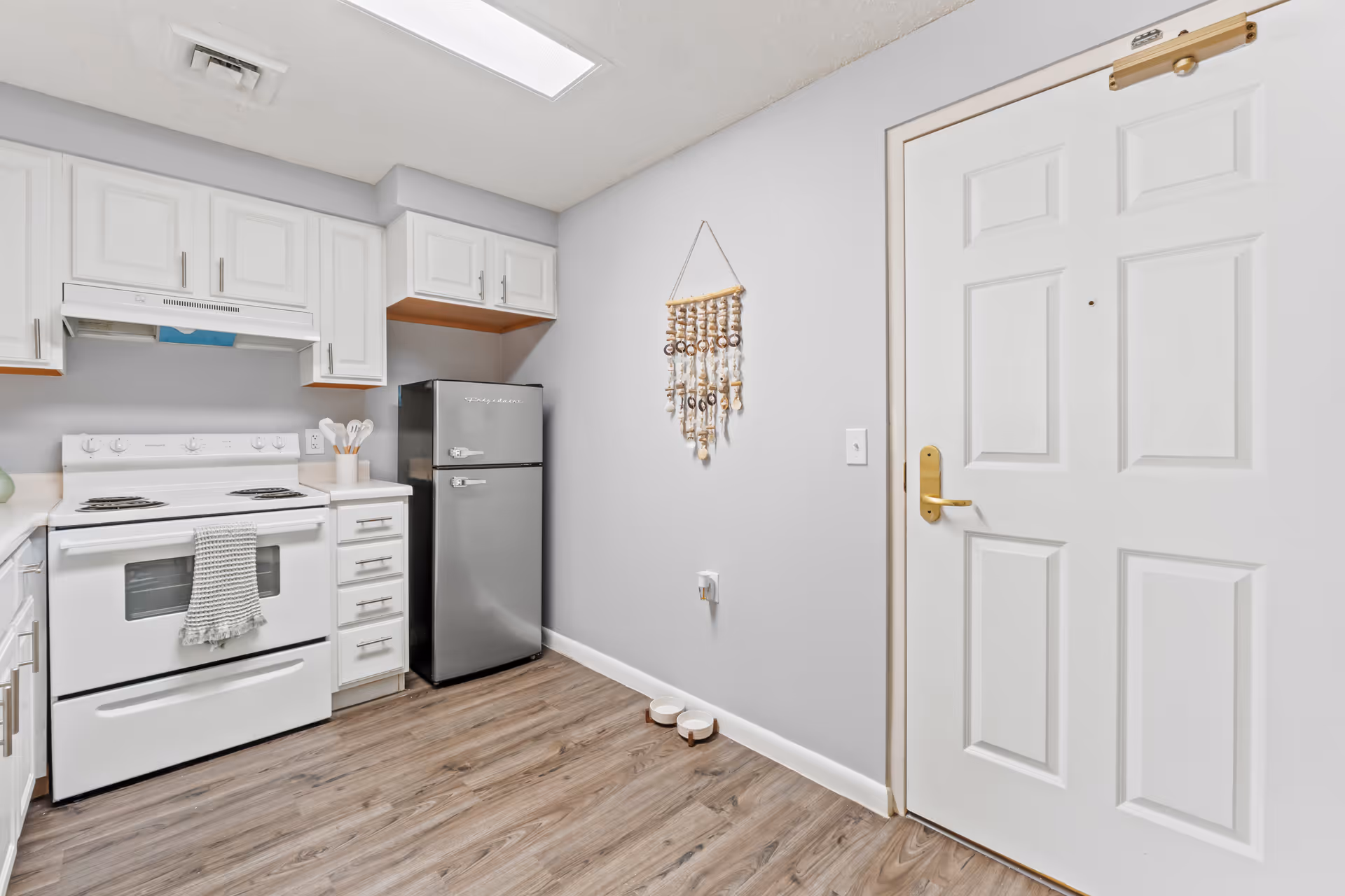 White kitchen with stove, refrigerator, cabinets, and doorway in a senior living unit.