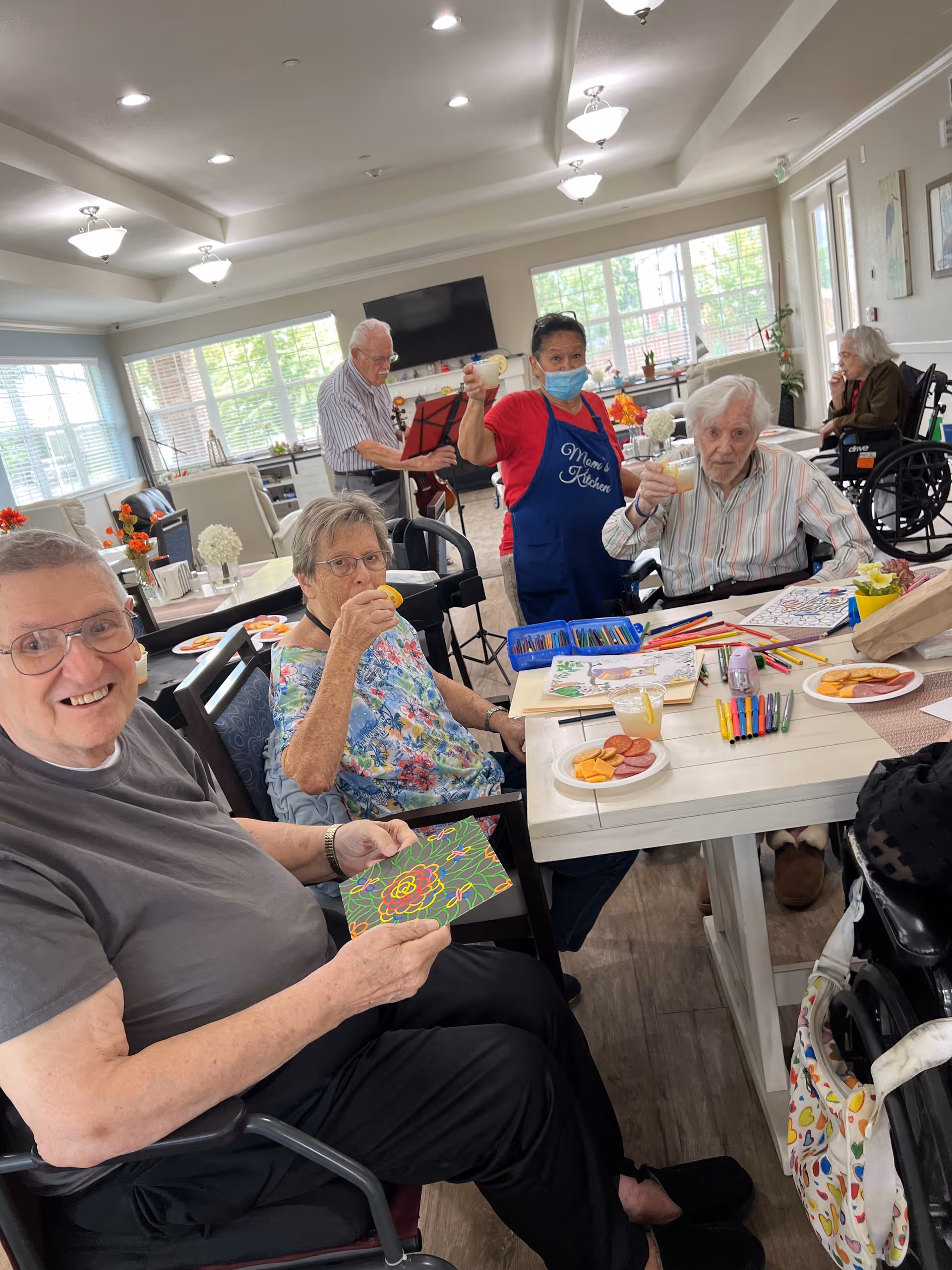 Residents and staff gather around a table for a craft activity in a bright communal room.