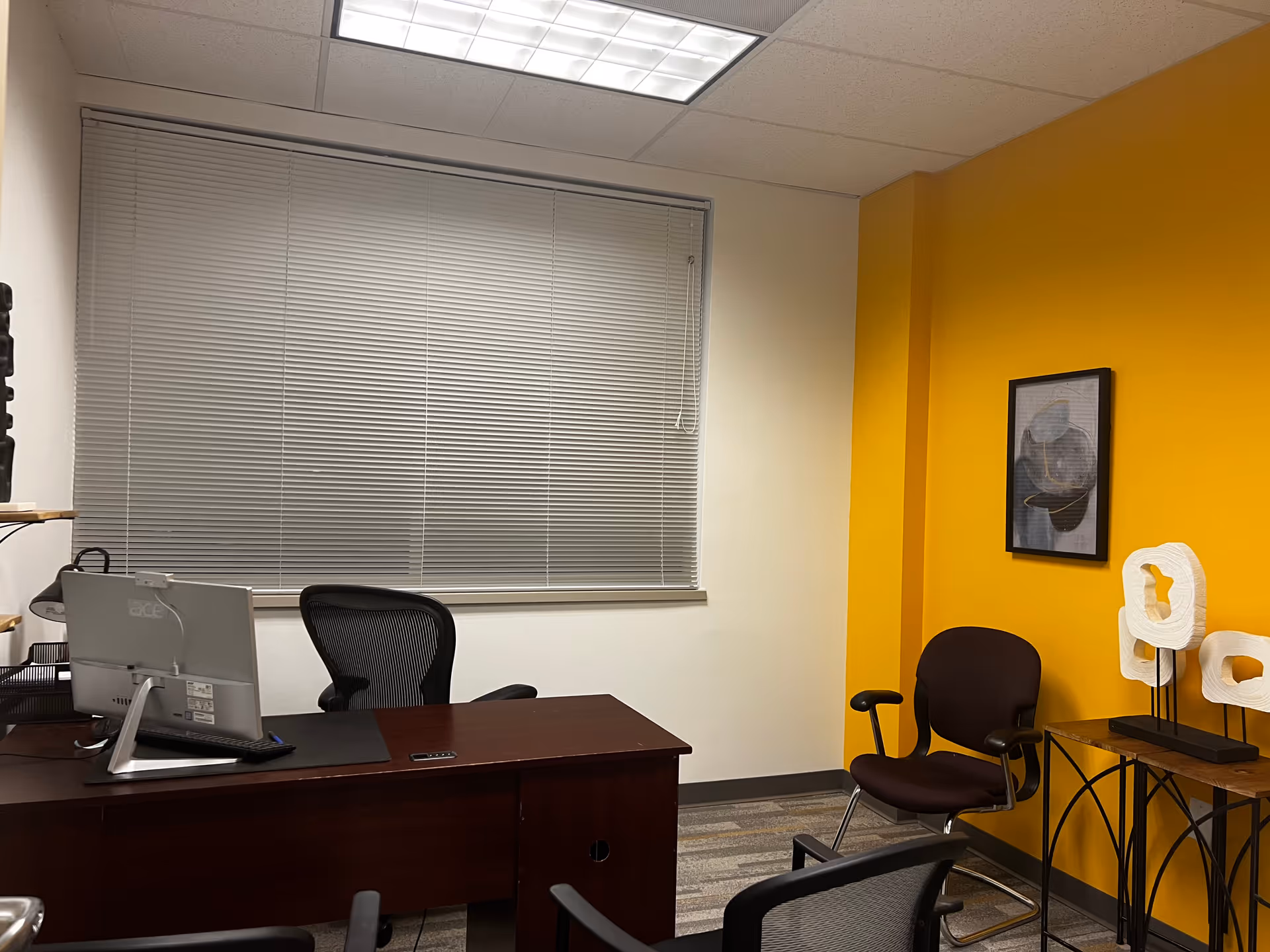 Desk with computer and chairs in a bright yellow-accented office.
