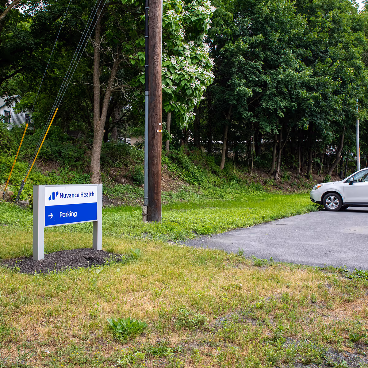 Outdoor view of Nuvance Health parking sign beside trees and a parked white car.