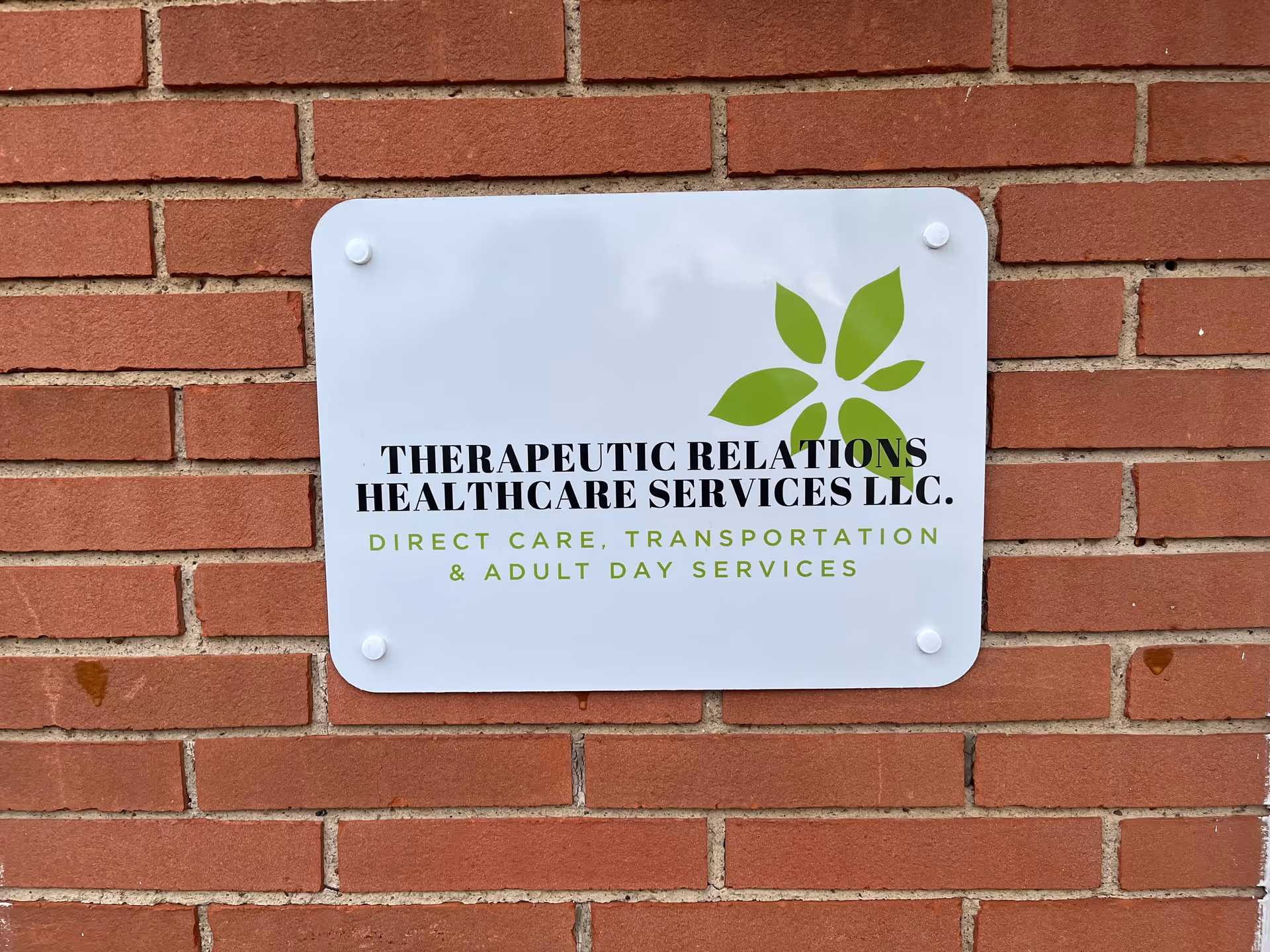 White rectangular sign with green leaf logo mounted on red brick exterior wall.