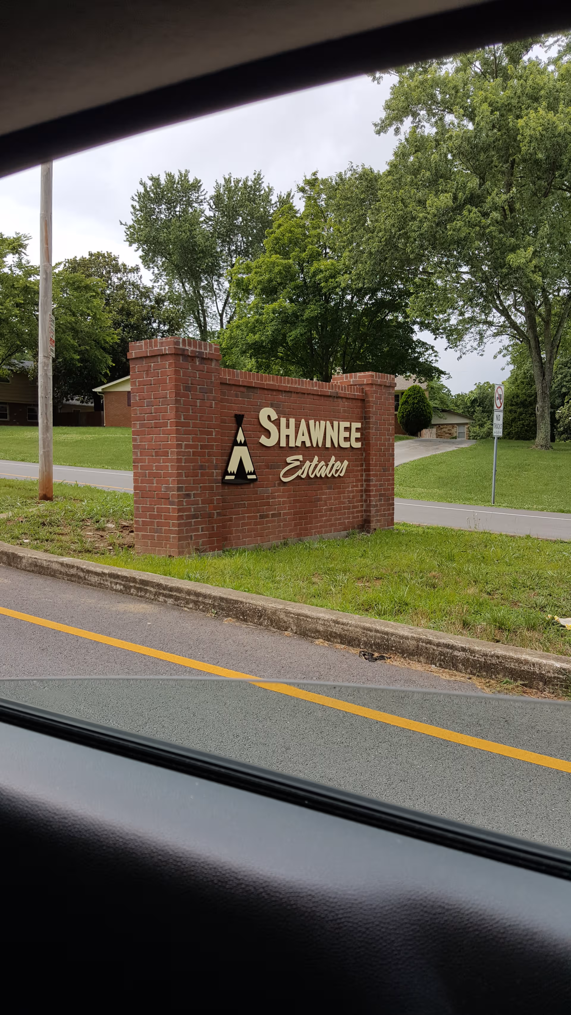 Brick Shawnee Estates sign on a grassy roadside with green trees.