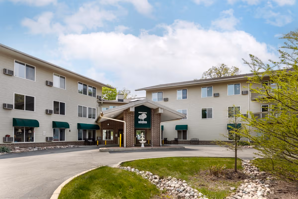 Exterior view of The Arboretum Senior Living building with green awnings and entrance canopy