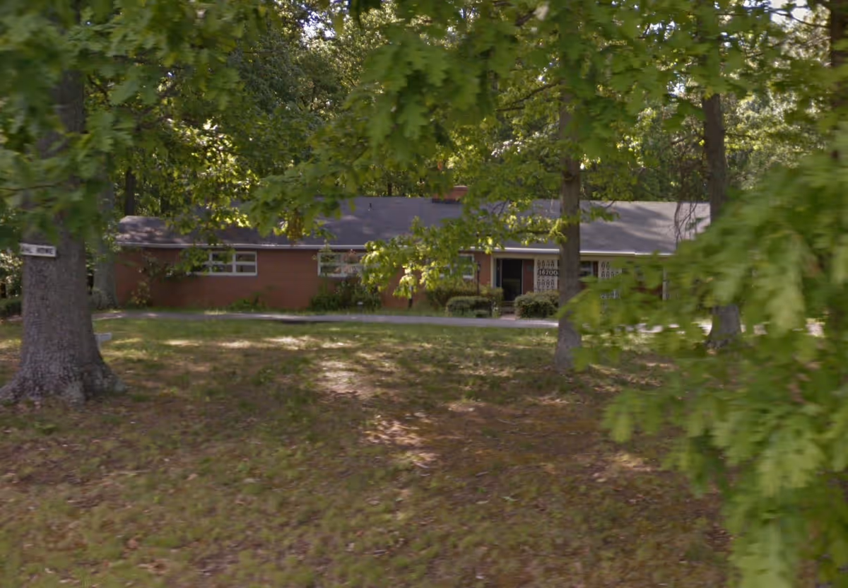 Exterior view of Ammahl Home for the Elderly, a single-story brick facility partly obscured by trees.