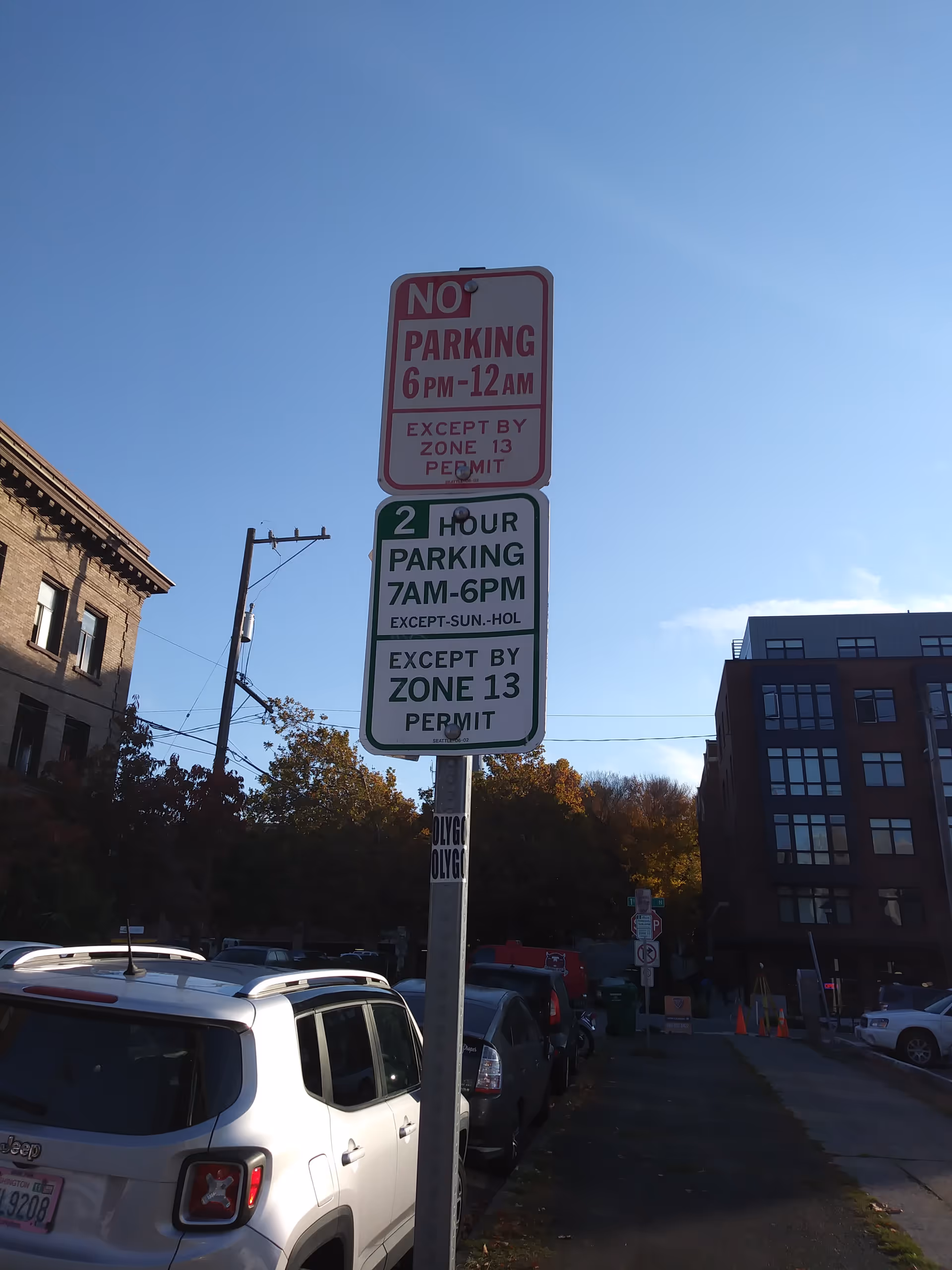 Exterior street scene with parked cars and multiple no-parking and permit signs near buildings.