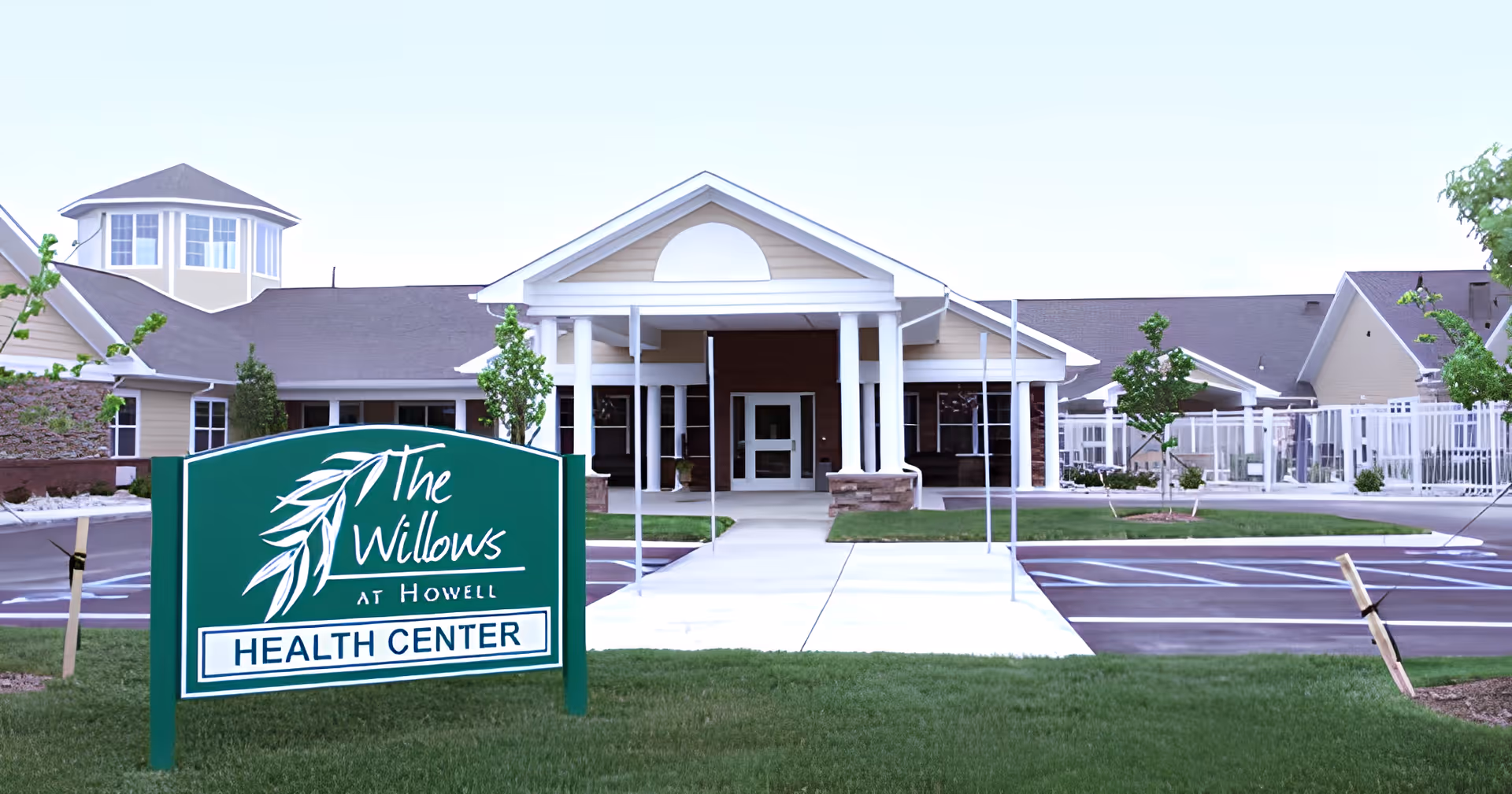 Front entrance of The Willows at Howell health center with a green sign on the lawn, a walkway, and a covered entry porte-cochère.