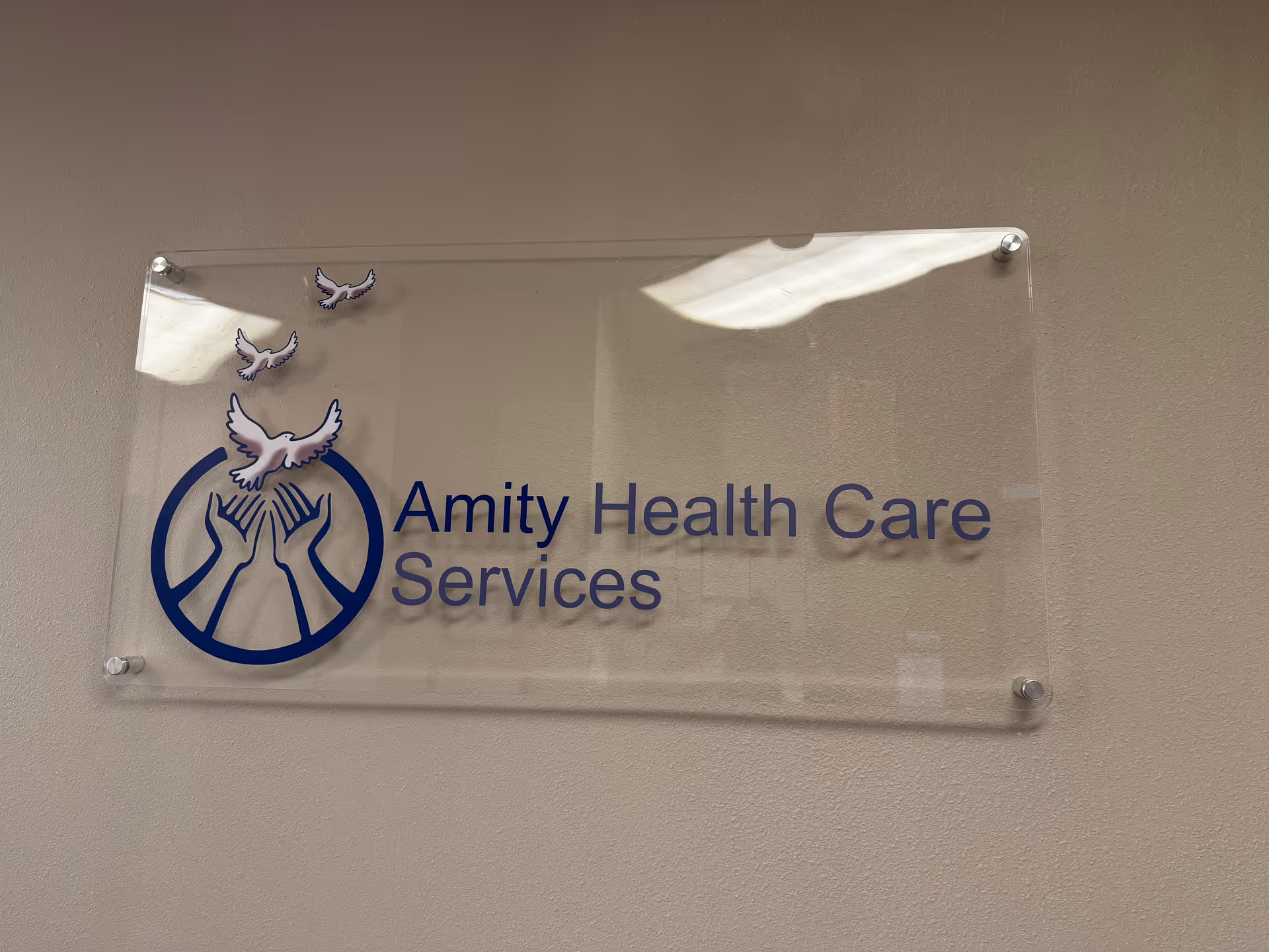 Clear acrylic wall sign displaying the Amity Health Care Services logo.