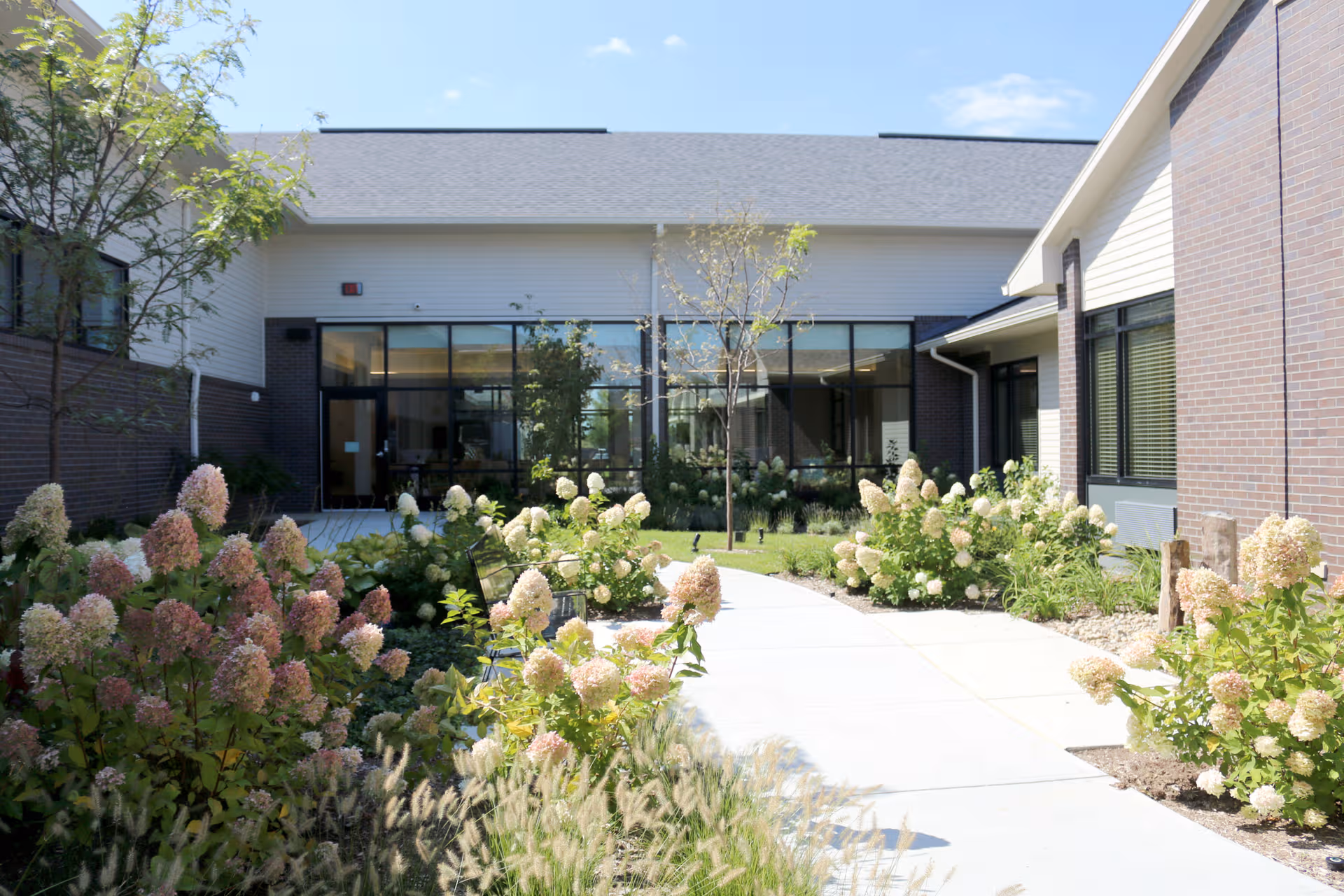 Exterior courtyard of a senior living facility with glass entrance doors and landscaped shrubs.