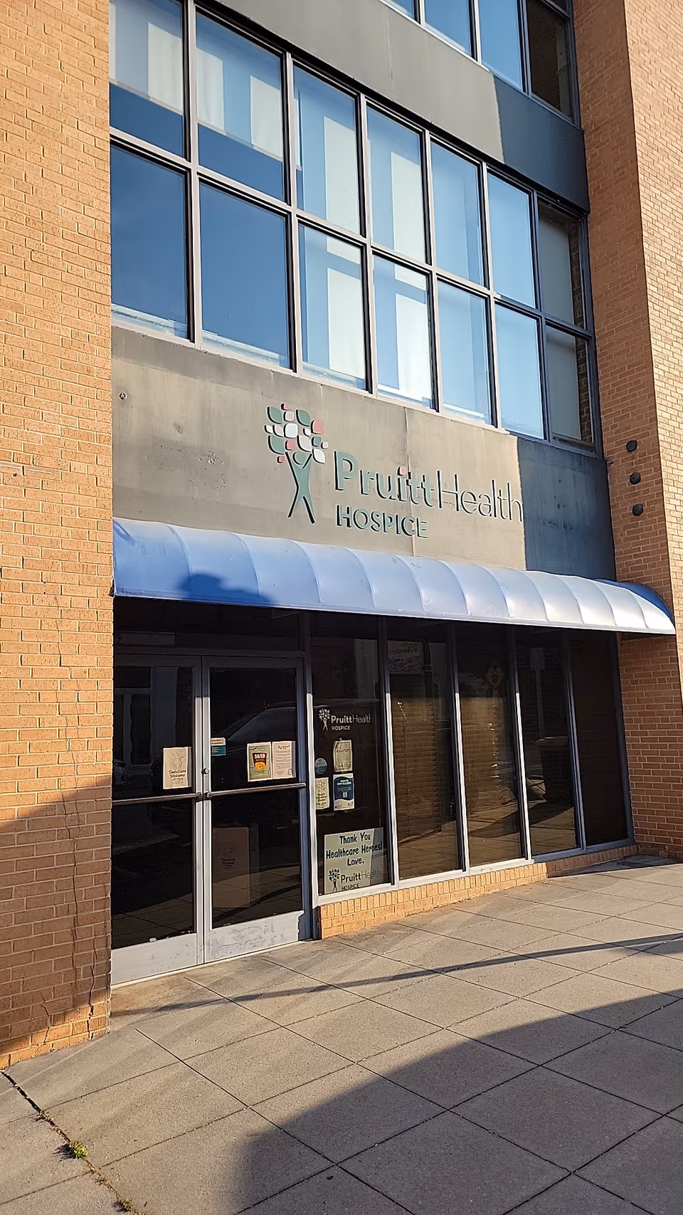 Exterior view of PruittHealth Hospice entrance with a blue awning and glass doors.