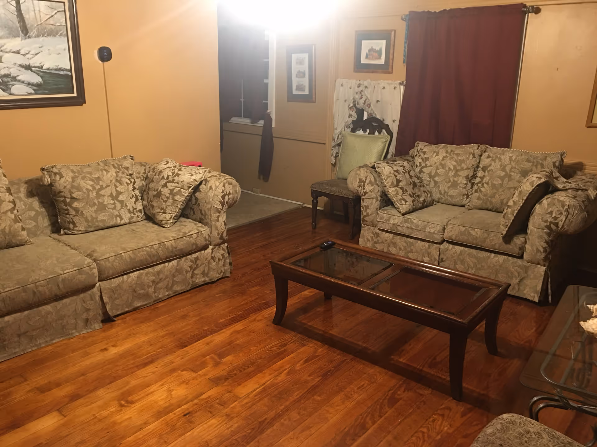 Two floral sofas surround a glass coffee table in a cozy living room.