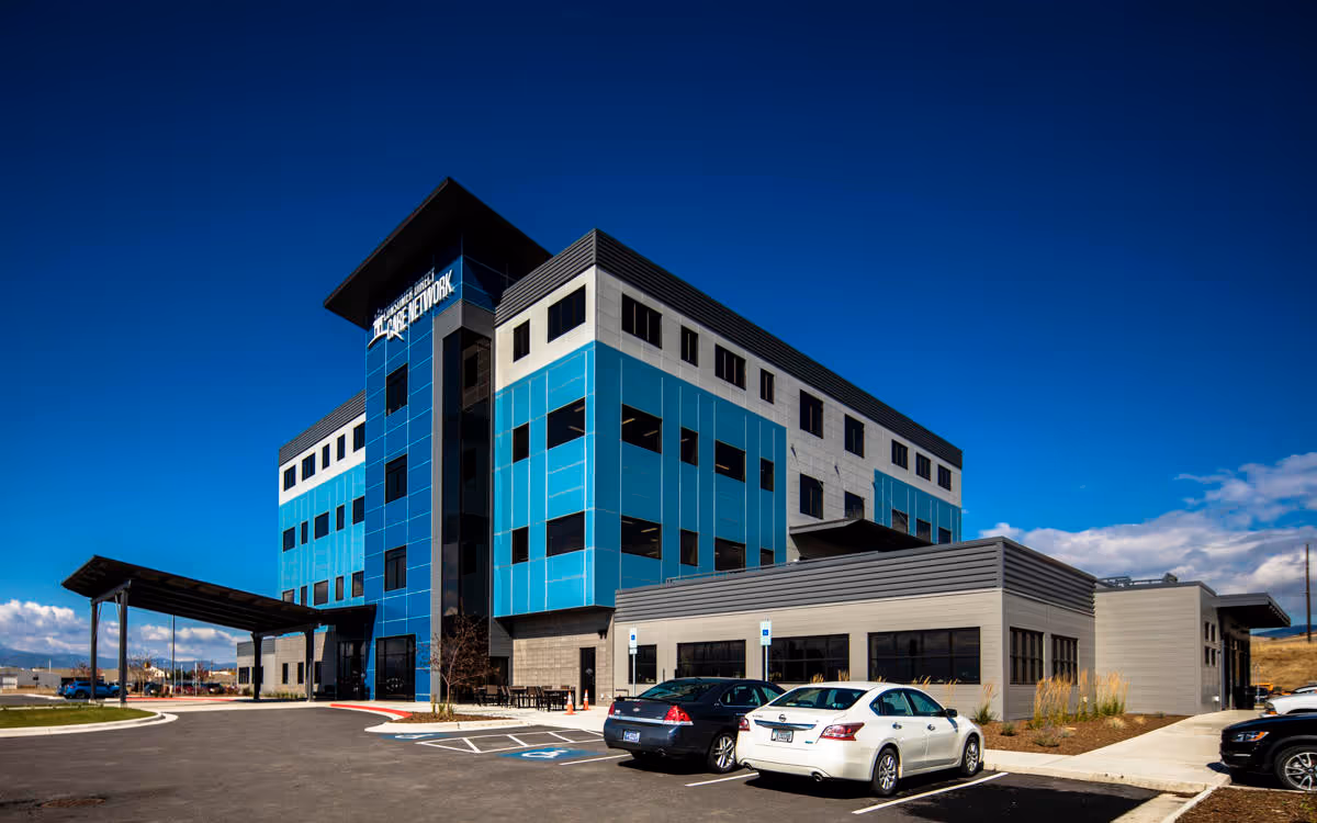 A modern blue-gray multi-story building exterior with parked cars and a clear blue sky.