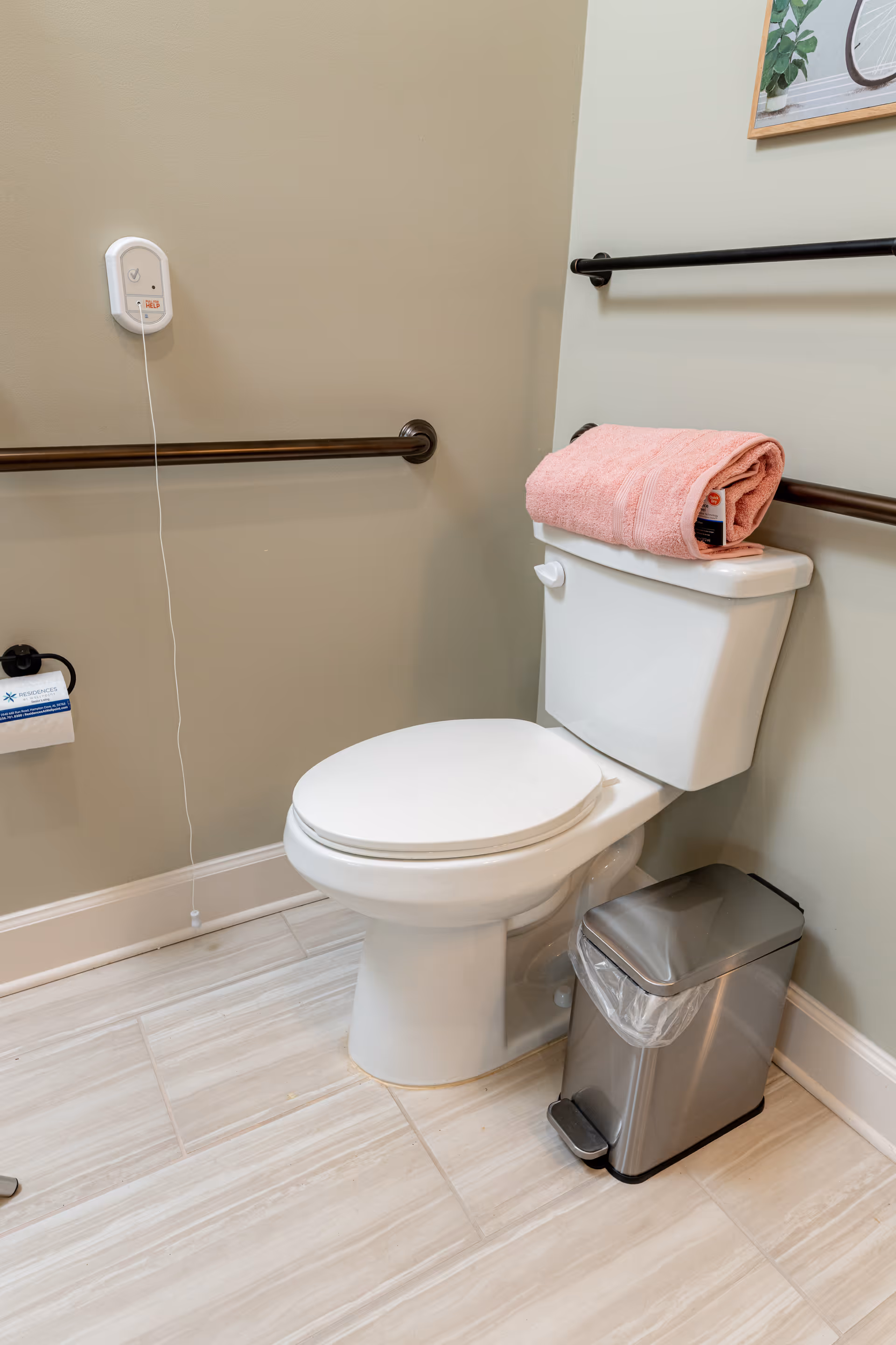 Accessible bathroom with toilet, pink towel, grab bars, and a small trash can.