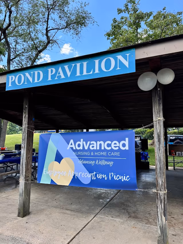 Outdoor pavilion with a Pond Pavilion sign and Advanced Nursing & Home Care picnic banner.