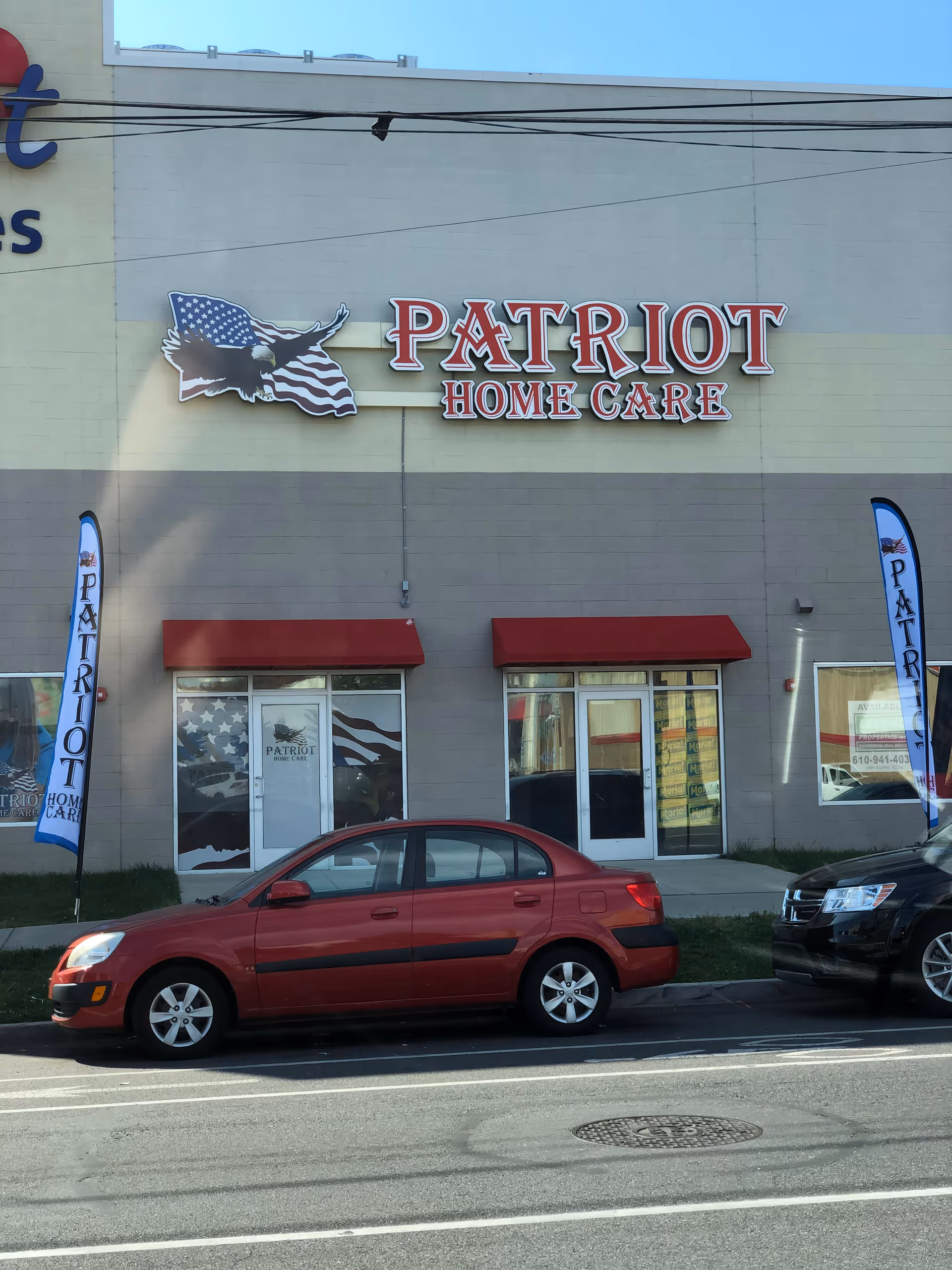 Exterior of Patriot Home Care building with sign, windows, red awnings, and parked cars.
