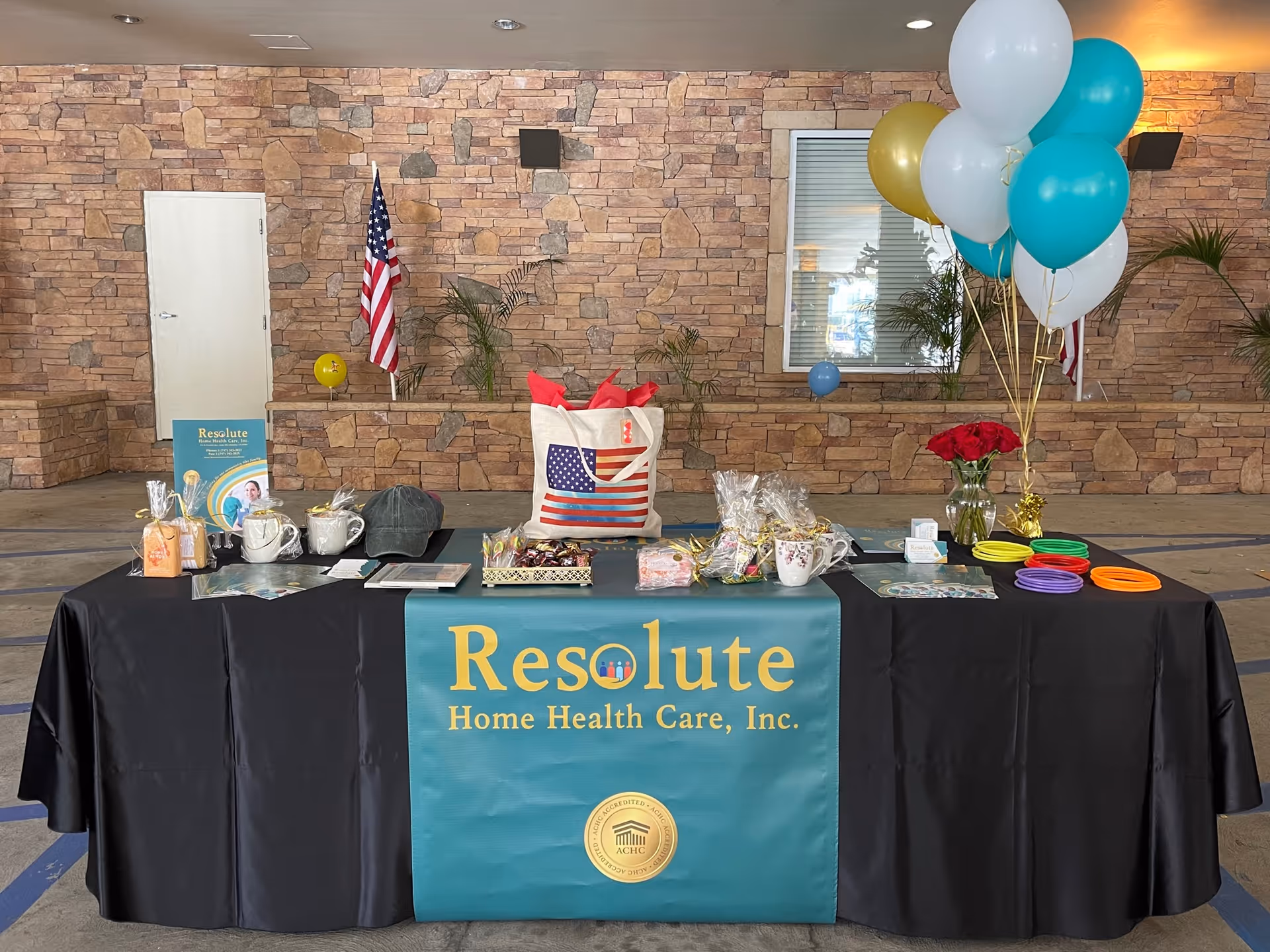 Indoor promotional table with Resolute Home Health Care banner, balloons, and gift items.