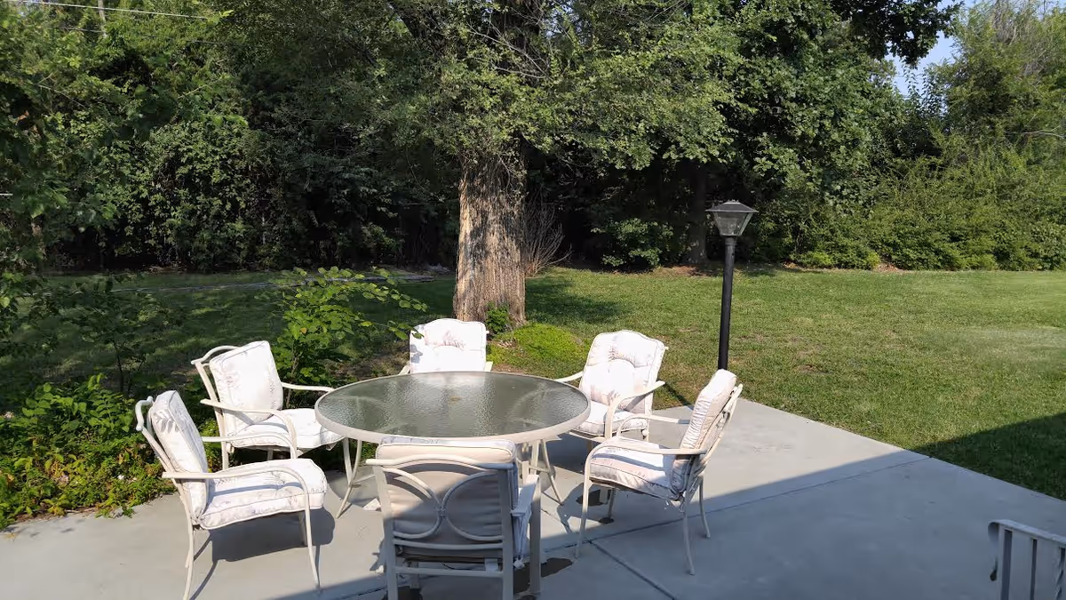 White cushioned outdoor patio furniture surrounds a glass round table in a grassy yard.