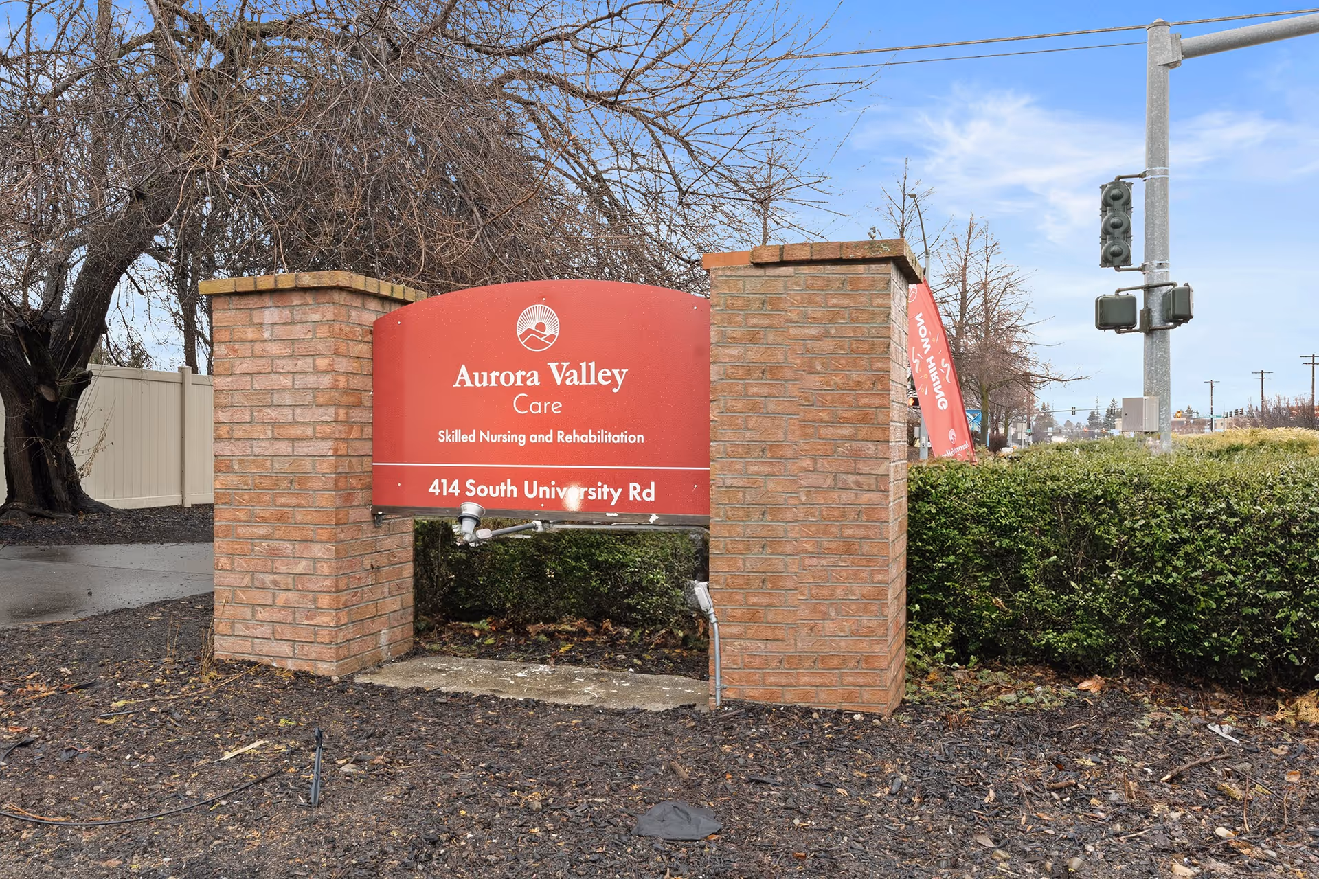 Red brick entrance sign for a care facility with hedges and trees nearby.