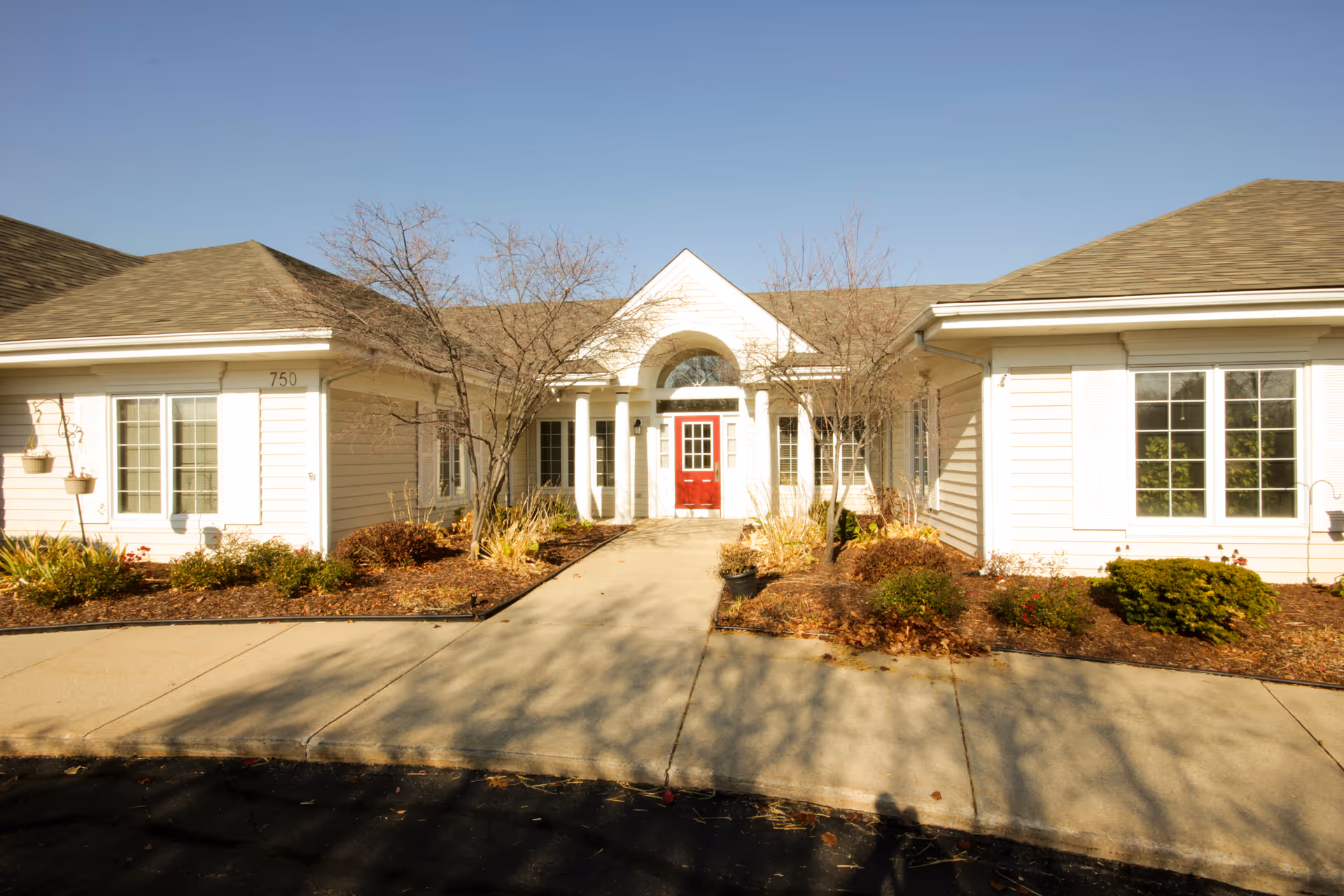 White, single-story senior living building with a red front door and landscaped entrance.