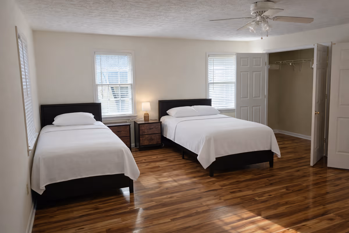Two single beds with nightstands in a bright bedroom beside an open closet.