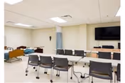 An empty conference room in a senior facility with chairs, a TV, and beds visible.