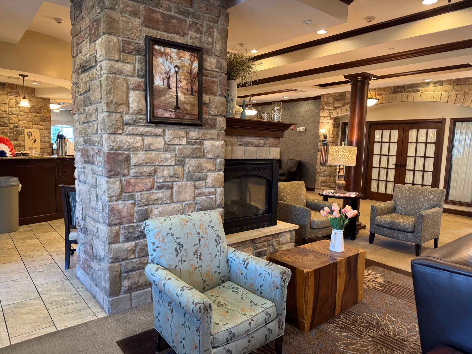 Stone fireplace anchors a communal seating area in a warm senior living lounge.