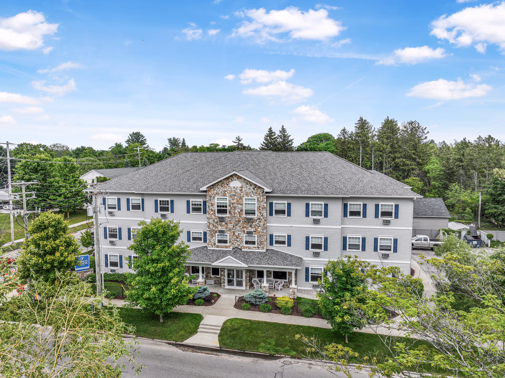 A multi-story senior living building with a stone central facade and surrounding trees.
