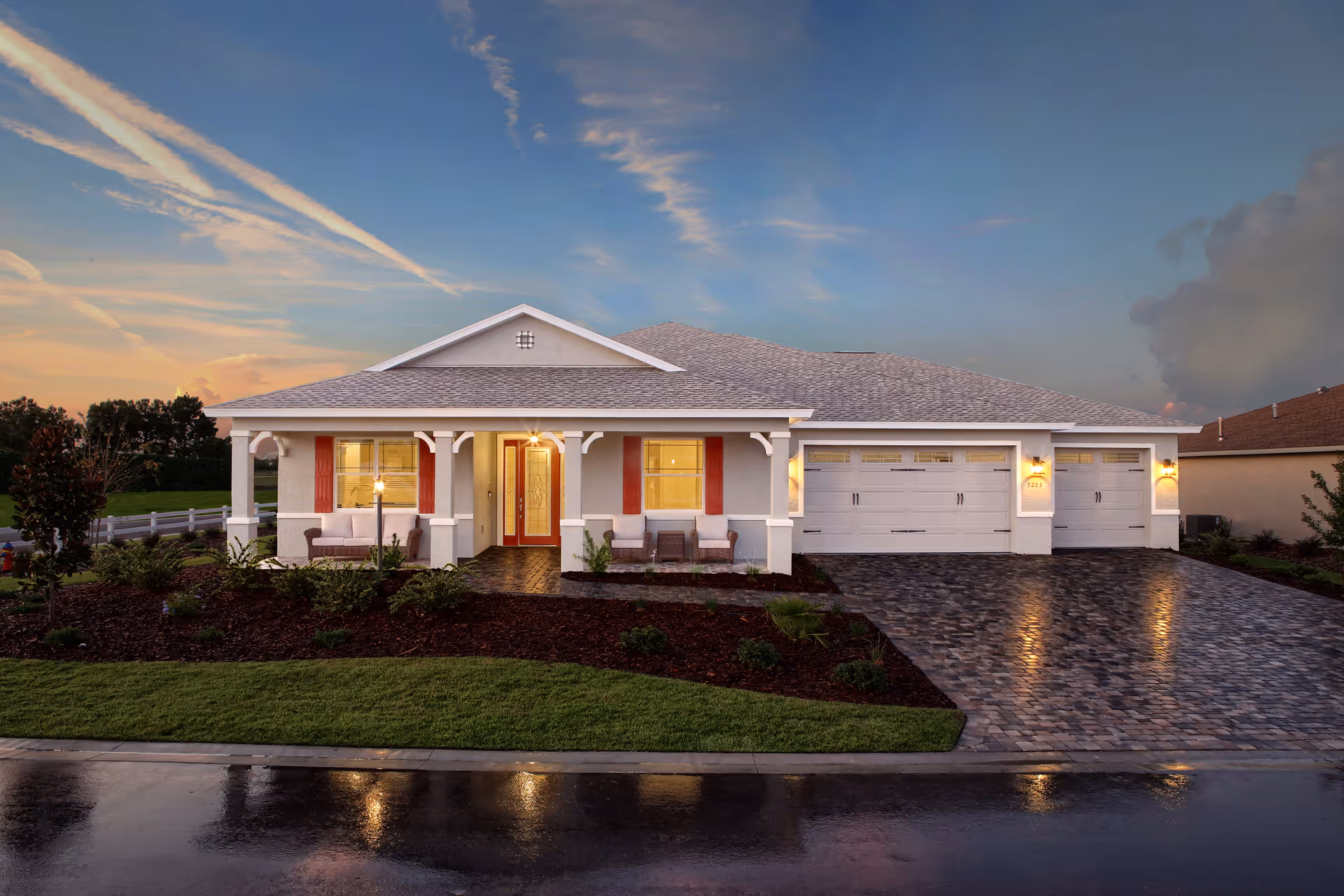 Single-story house with a covered front porch, lit windows, and a three-car garage at dusk.